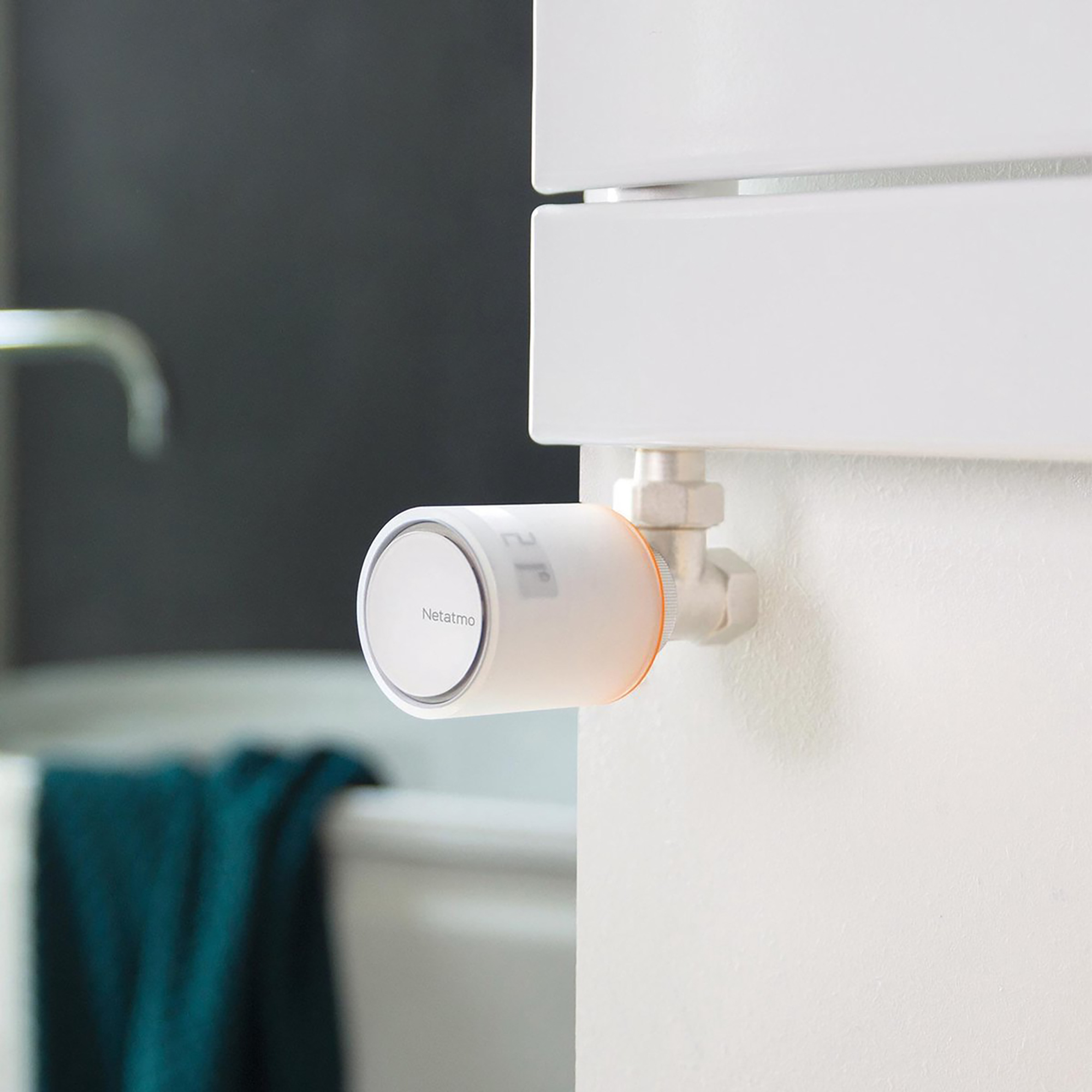 White smart thermostat on a white wall next to a white radiator. Orange ring around the device.