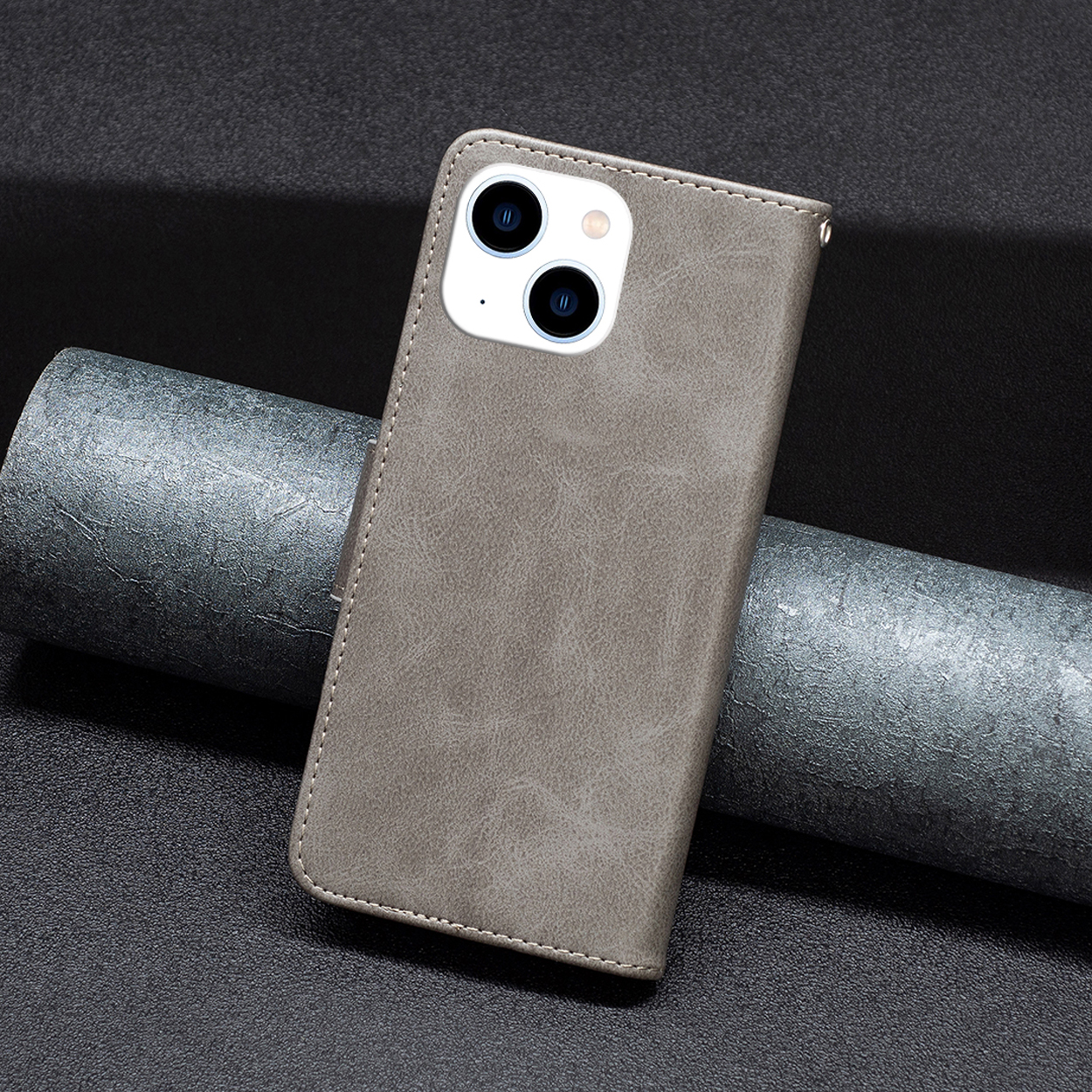 Een grijze telefoonhoes met een uitsparing voor de camera. De hoes ligt op een donker oppervlak met een metalen rol.