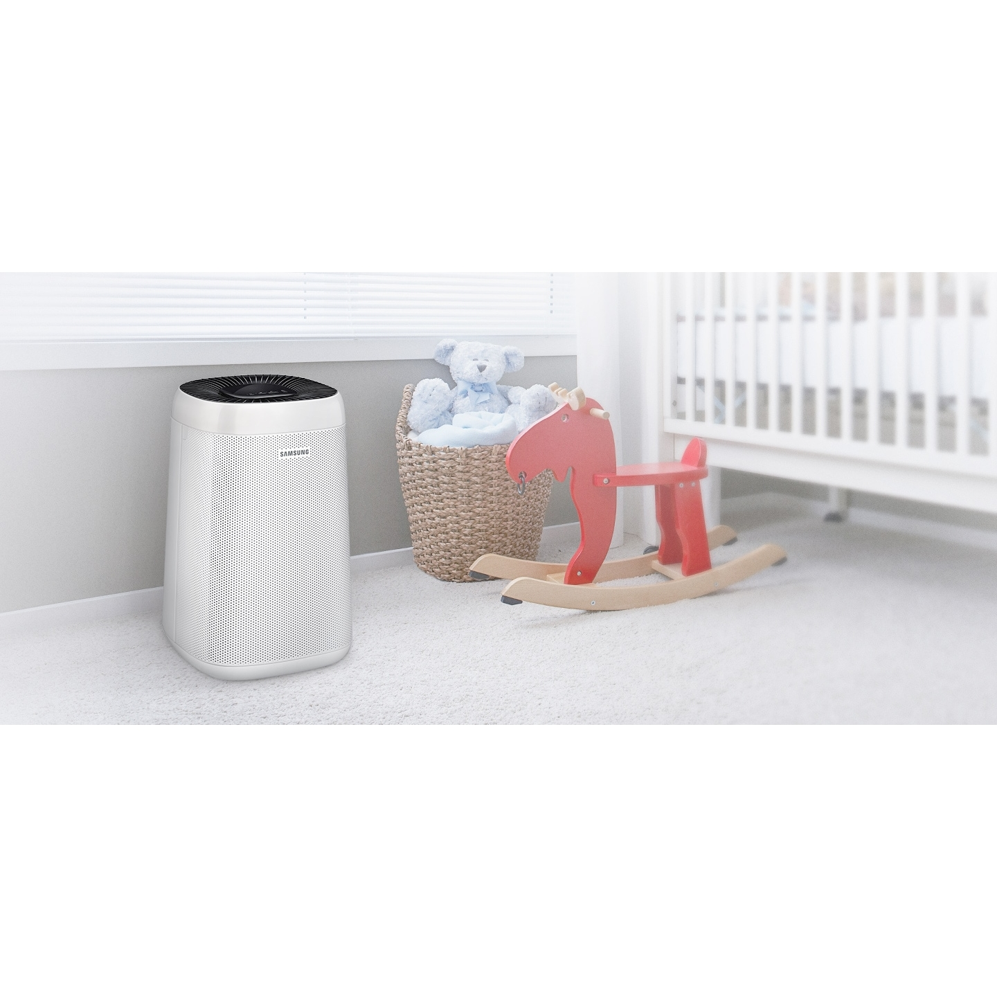 Ein weißer Luftreiniger im Babyzimmer. Es gibt ein Kinderbett, ein Schaukelpferd und einen Korb mit Teddybär.