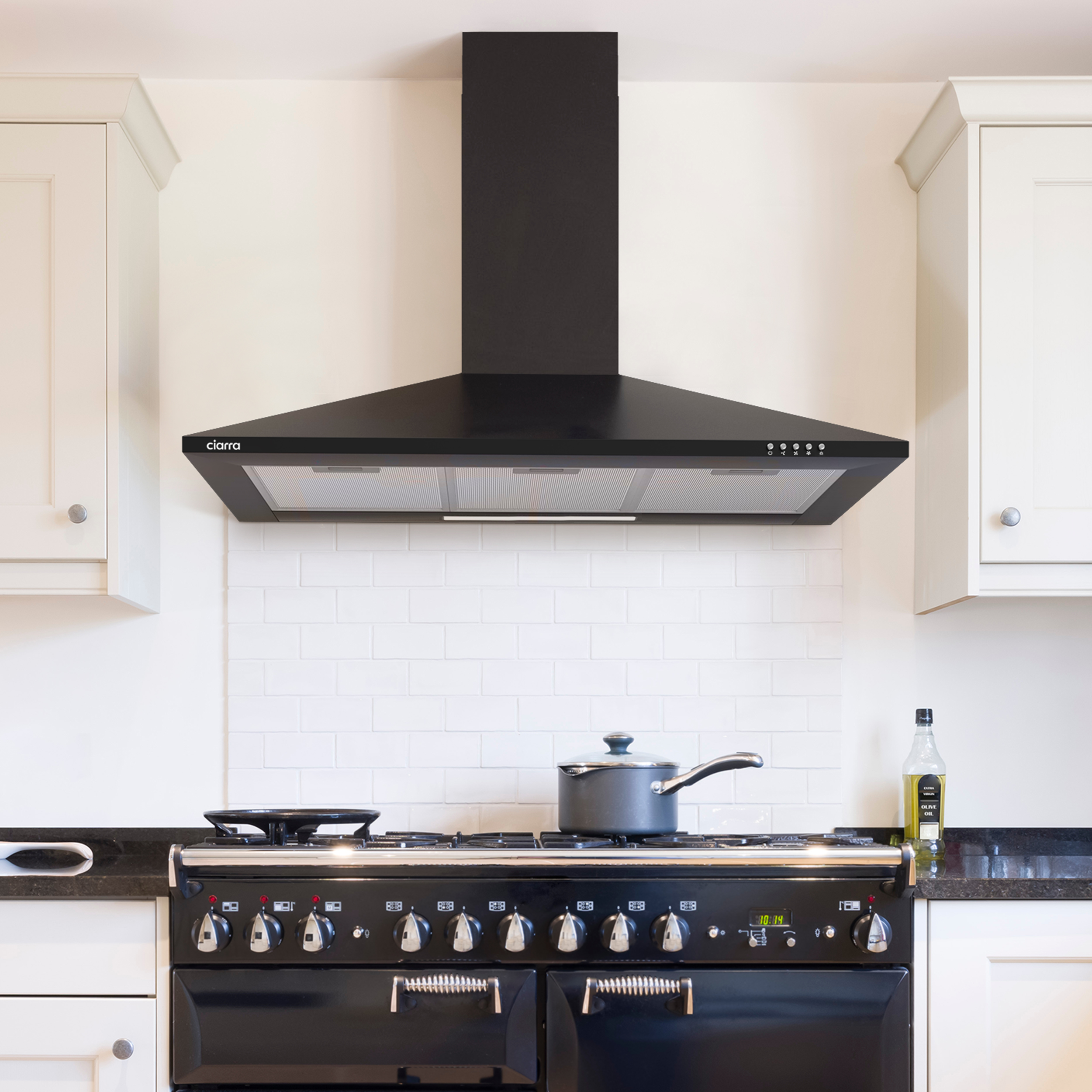 Keuken met zwart fornuis, afzuigkap en witte kasten. Een pan.