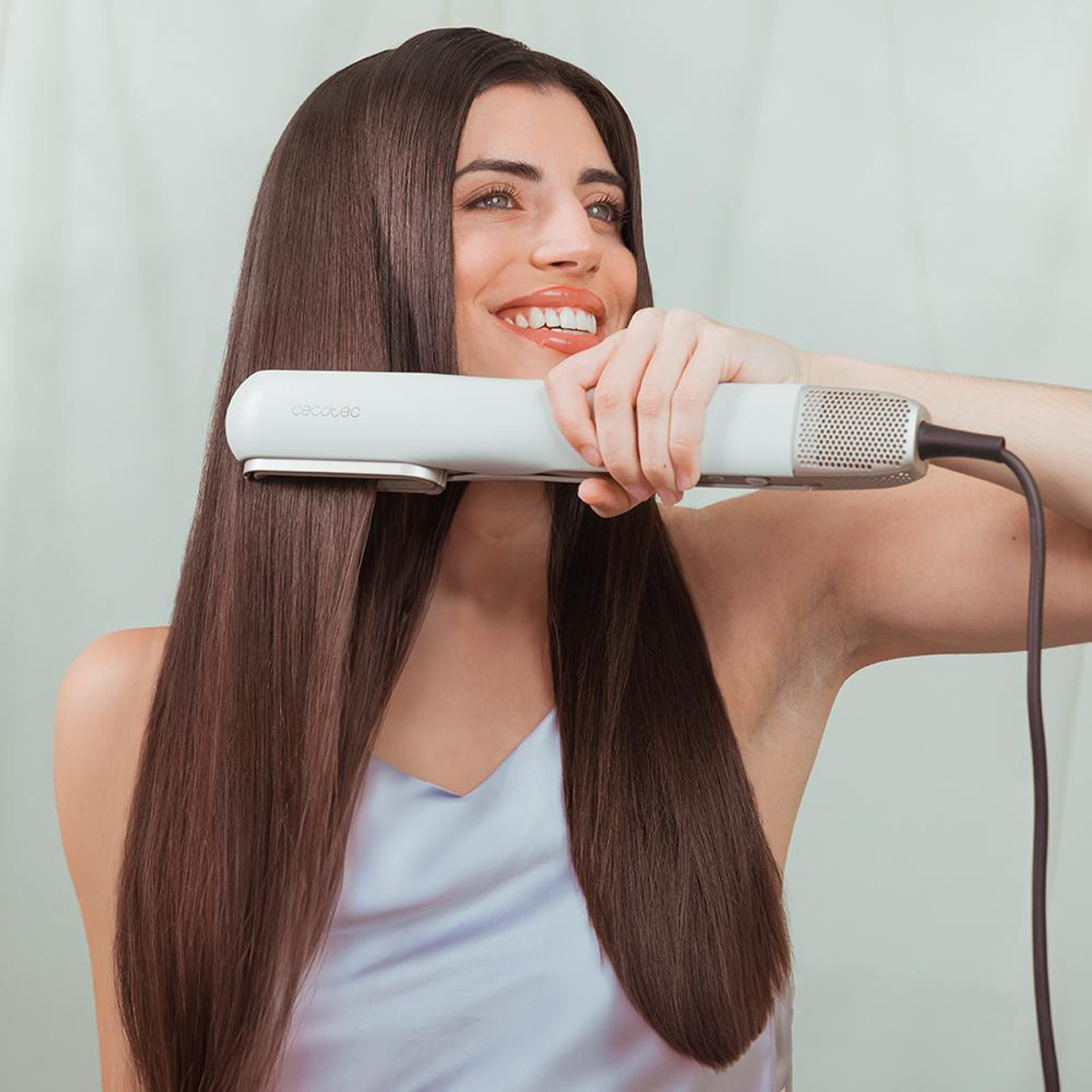 Frau mit langen Haaren benutzt Glätteisen, lächelnd.