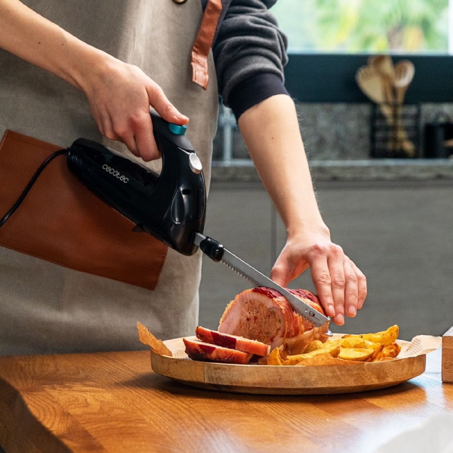Una persona está cortando un pastel de carne cocido con un cuchillo eléctrico. Hay un plato de madera con papas fritas.