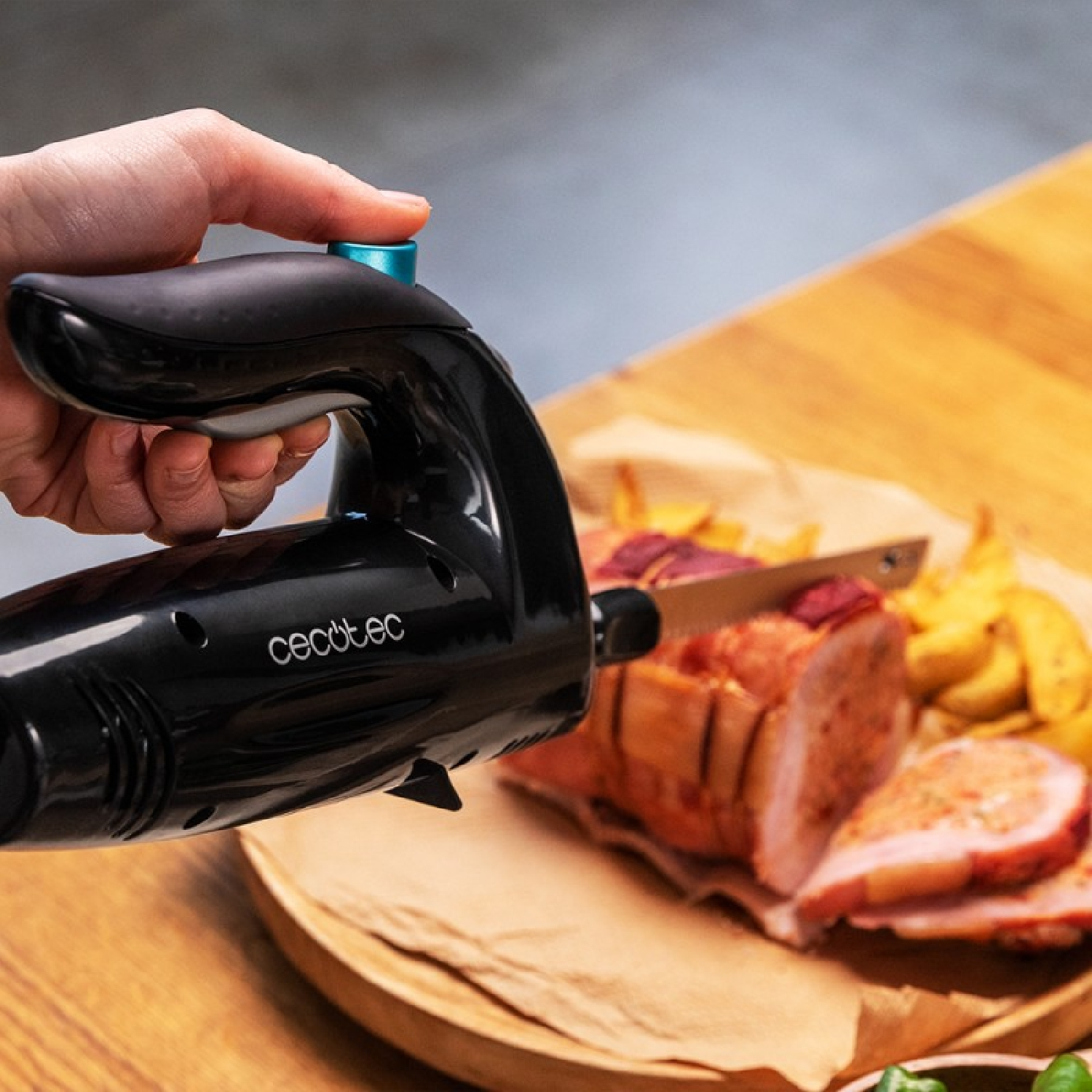 Mano usando un cuchillo eléctrico negro para cortar jamón cocido sobre tabla de madera.