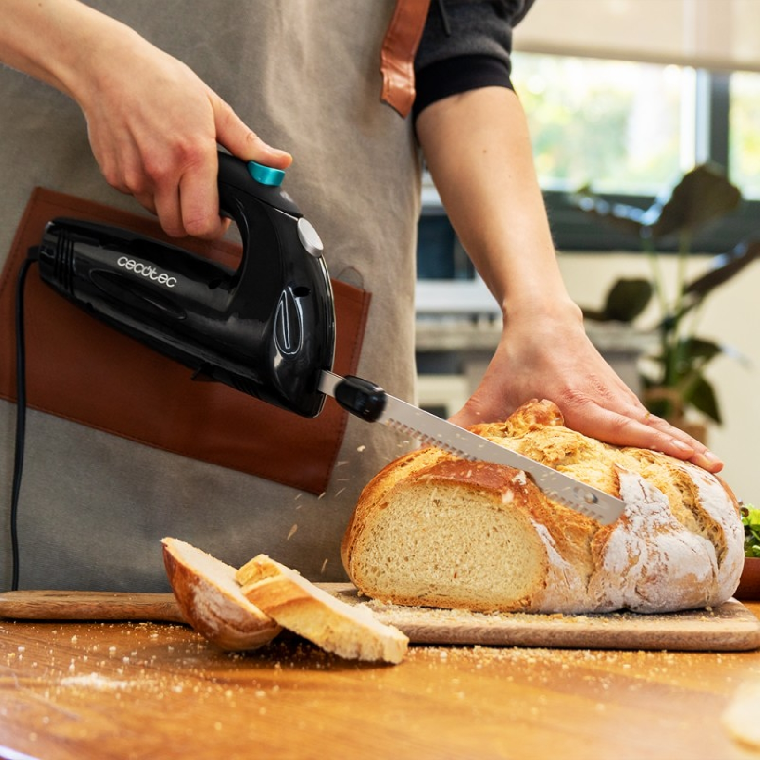 Persona cortando pan con un cuchillo eléctrico. Pan en una tabla de madera. Alfombrilla de cuero marrón.