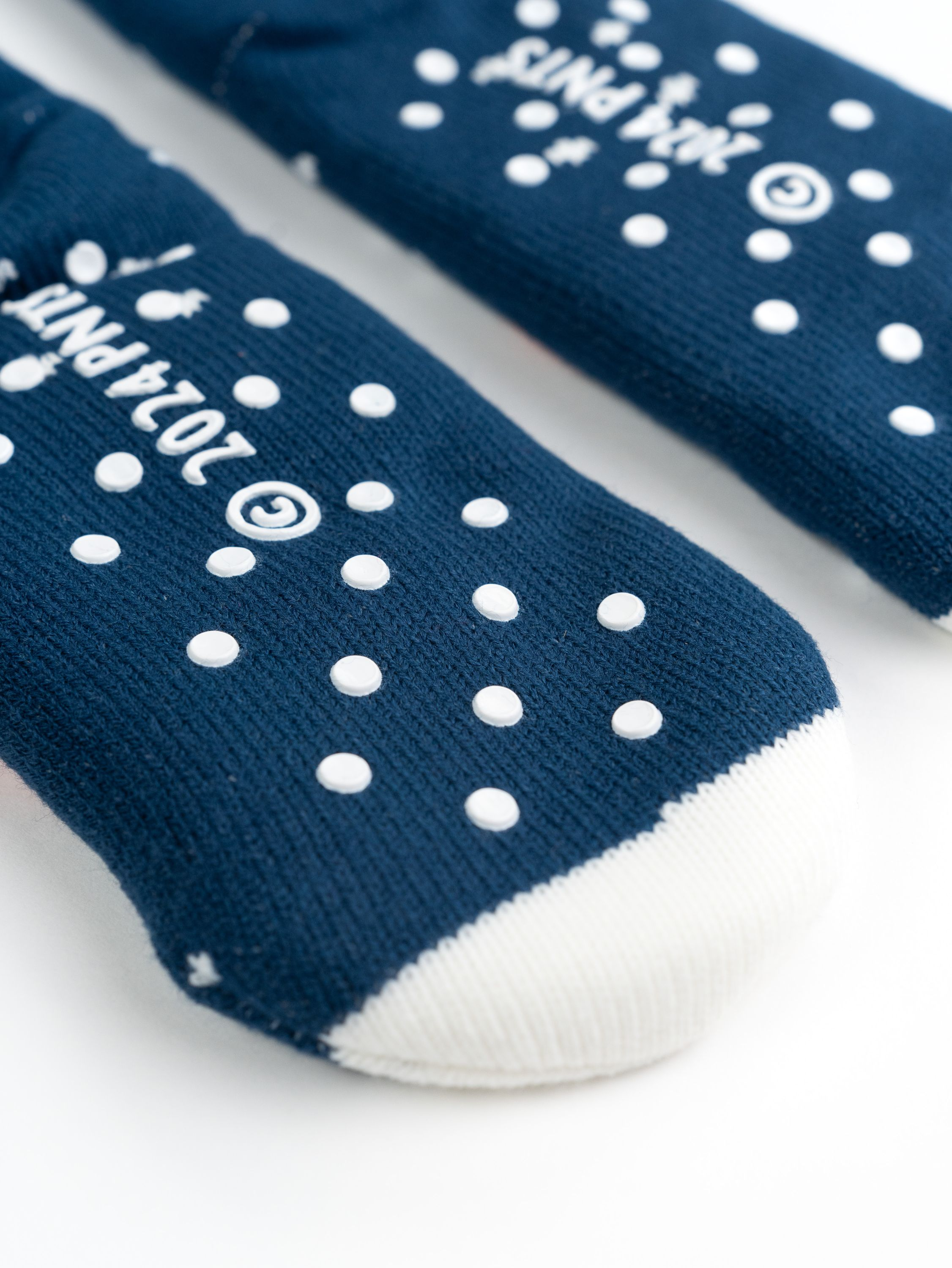 Socken mit weißen Punkten auf Dunkelblau. Text: 2024 PNTS, mit weißem Text und einer weißen Spitze.