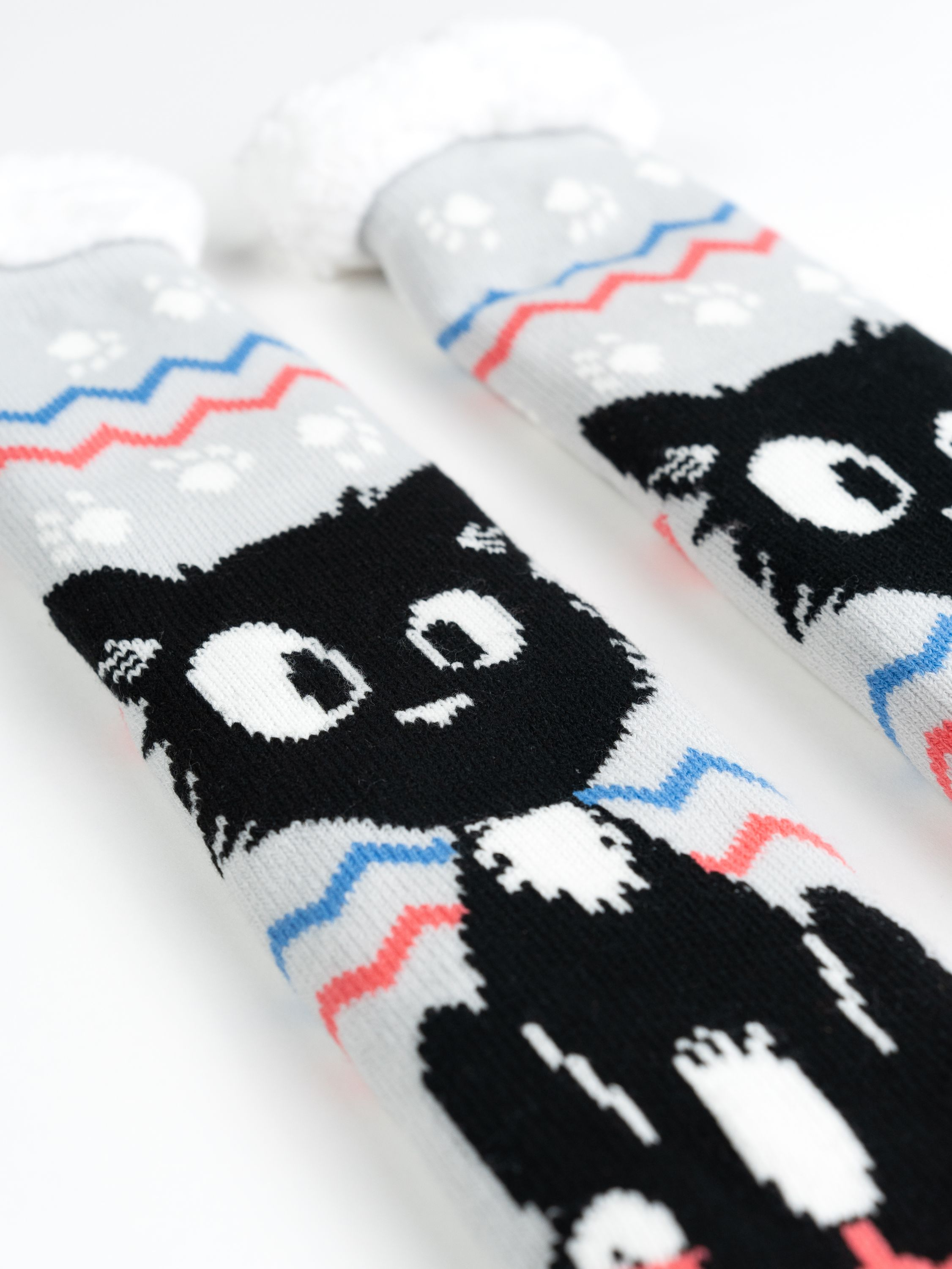 Zwei Katzensocken mit weißem Fellbesatz. Jede Socke hat ein schwarzes Katzengesicht.