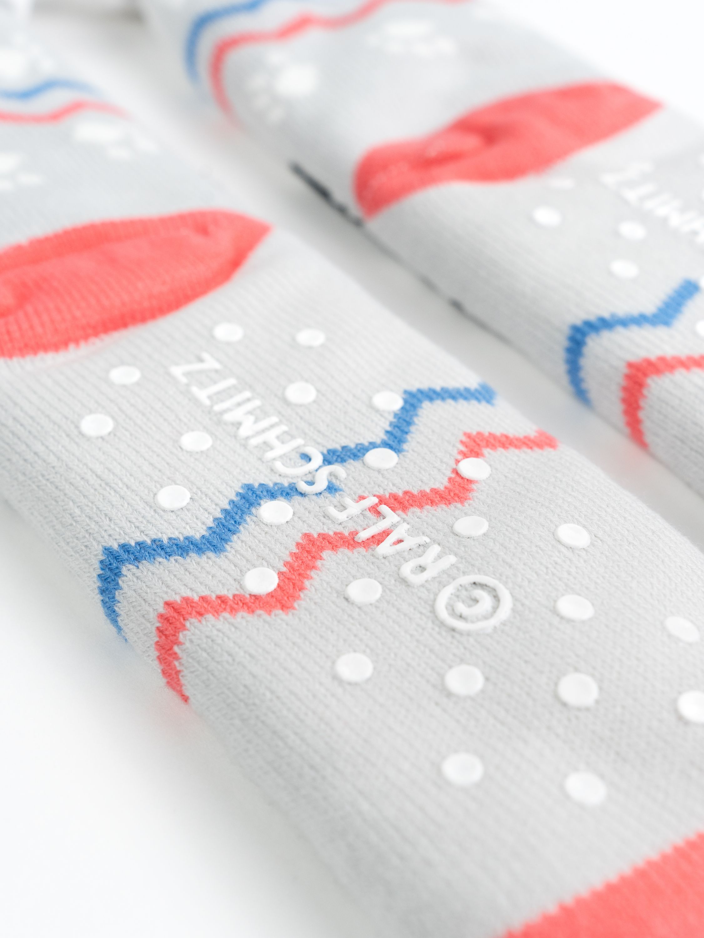 Nahaufnahme grauer Socken mit roten und blauen Zickzackmustern, weißen Punkten und Text.