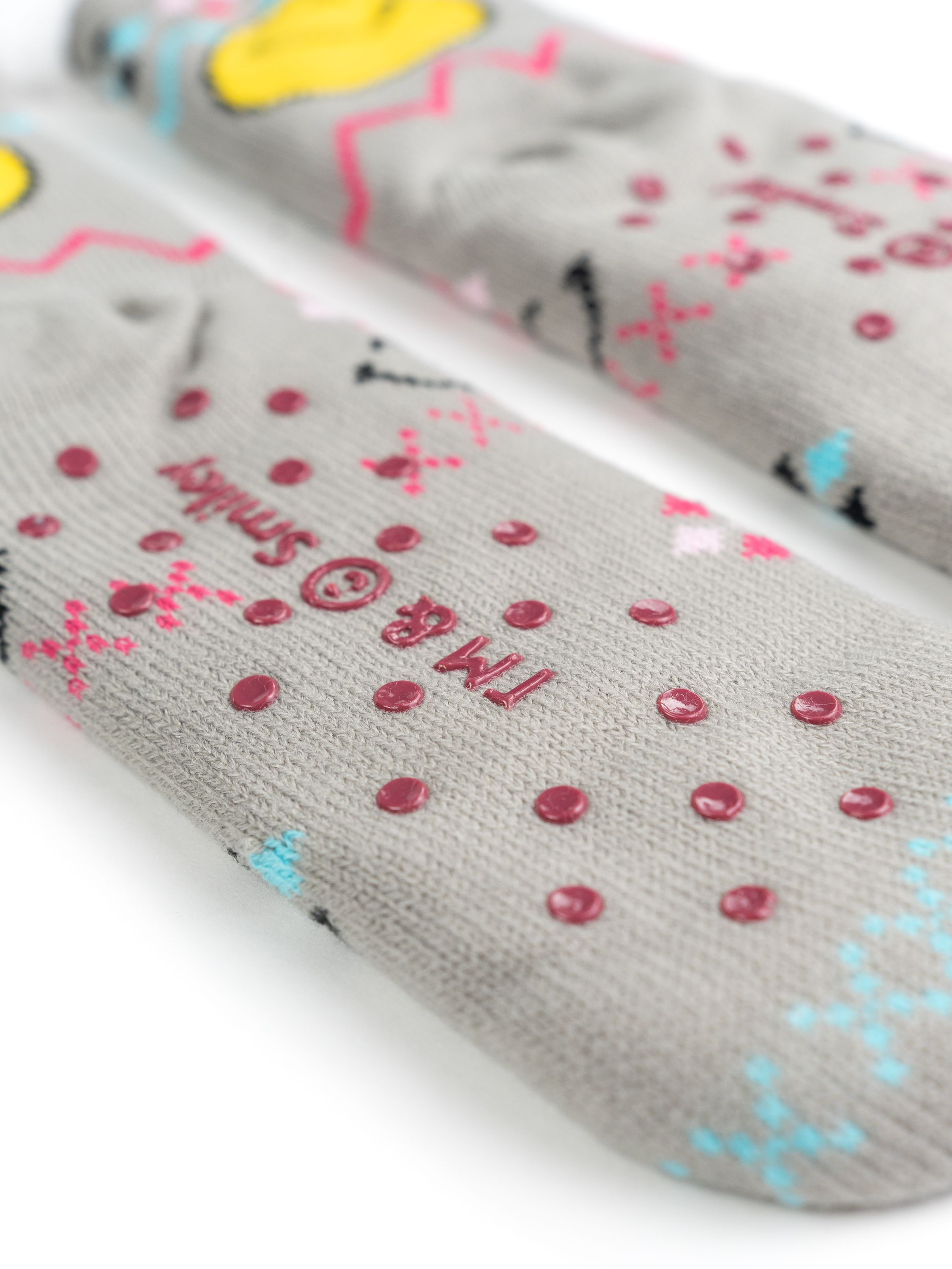 Nahaufnahme von grauen Smiley-Socken. Rote Punkte und rosa Muster sind auf der Sohle sichtbar.