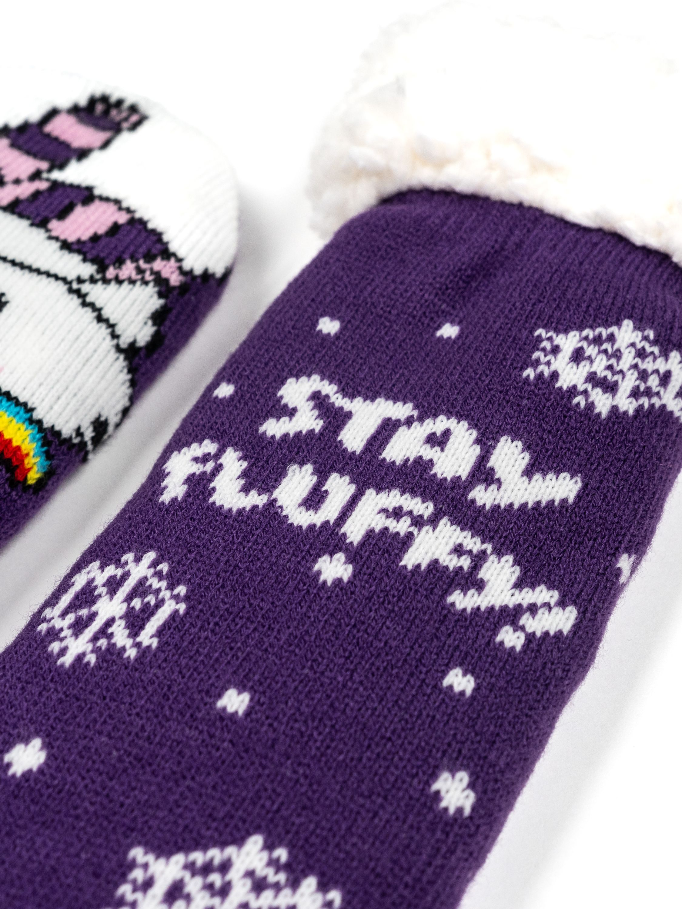 Lila flauschige Socken mit den weißen Worten „STAY FLUFFY“ und Schneeflocken. Weißer Hintergrund.