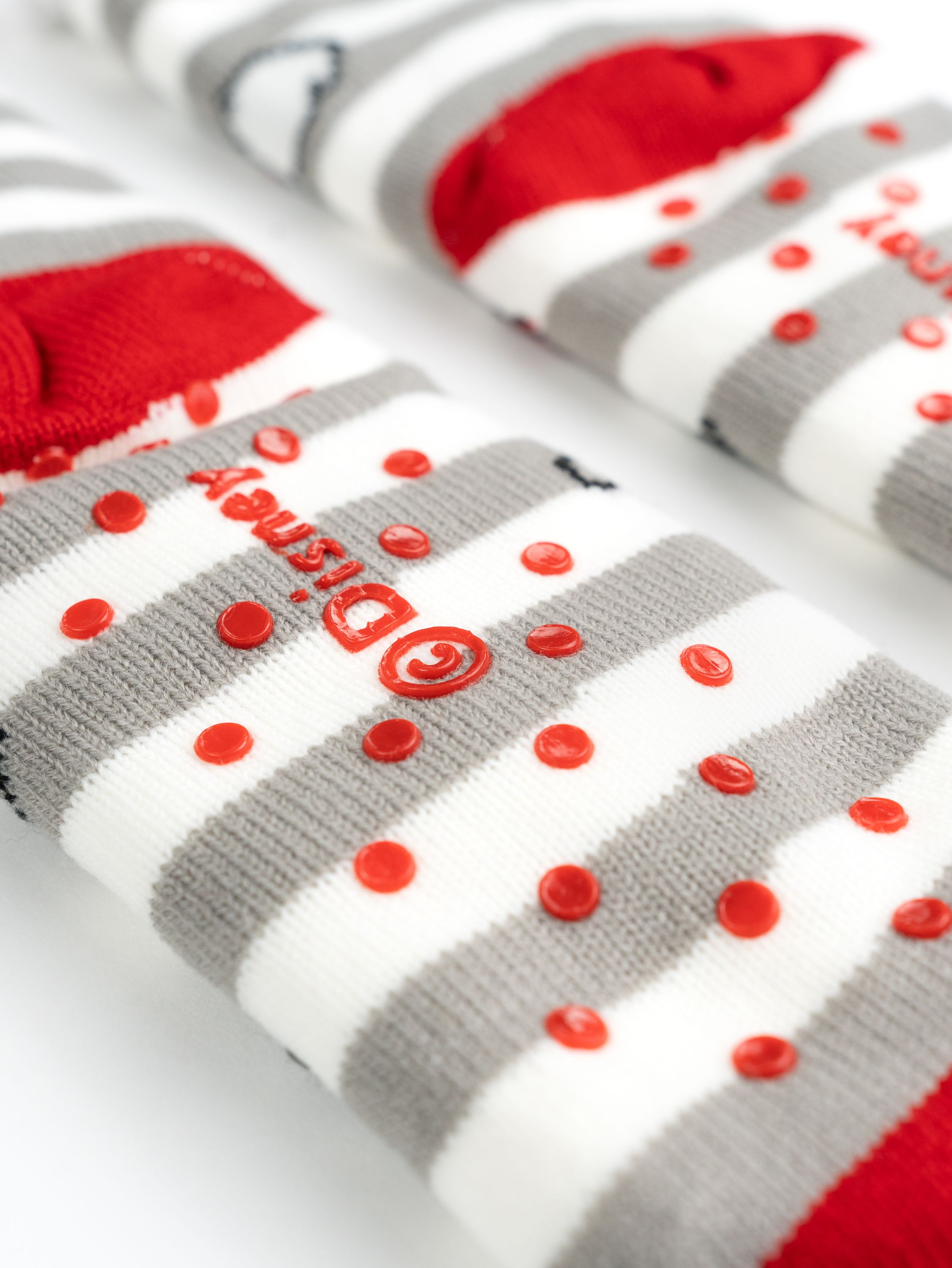 Nahaufnahme von gestreiften Socken mit roten Akzenten und roten Gummipunkten. Die Socken liegen auf weißem Untergrund.