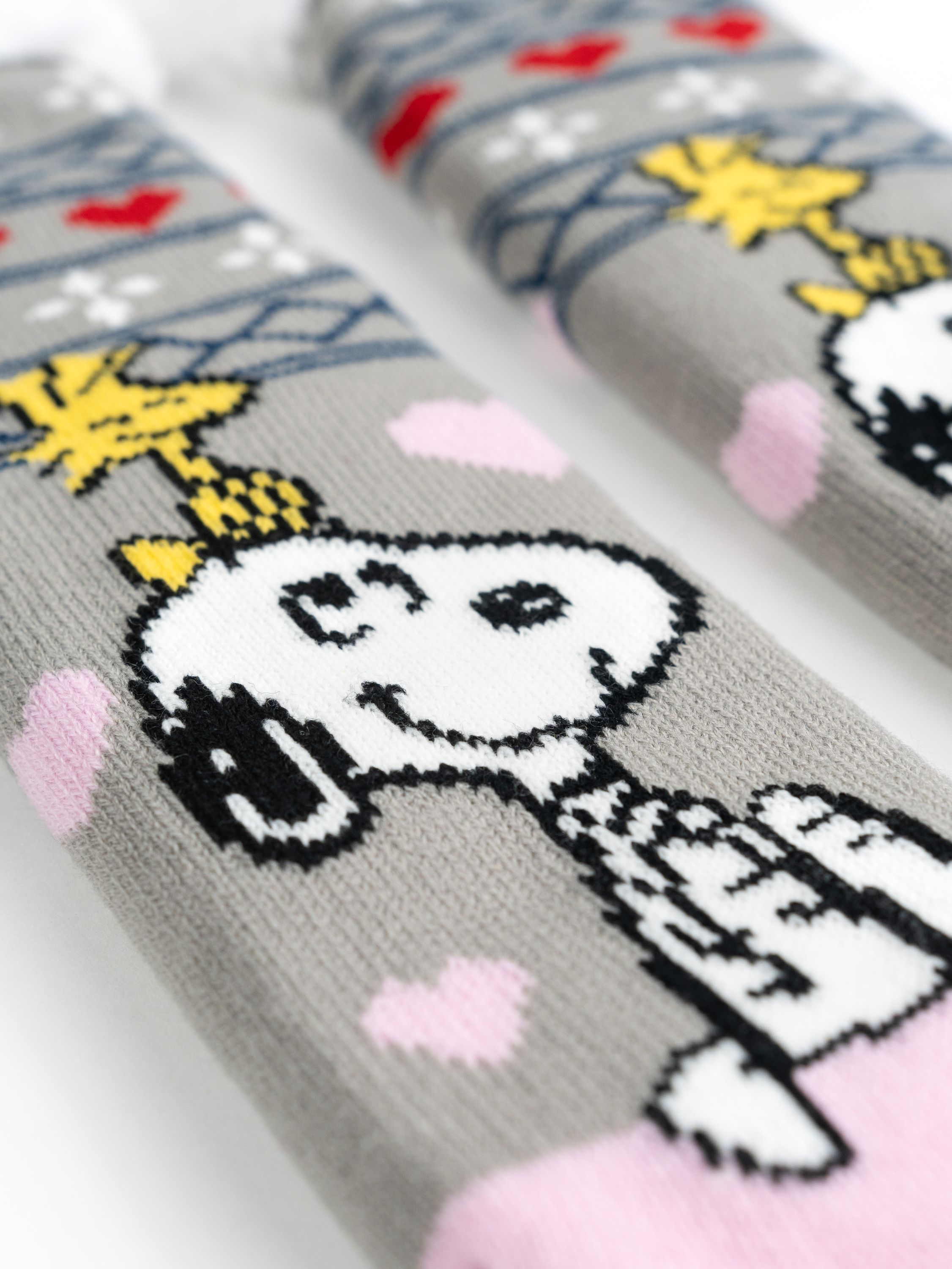 Nahaufnahme von zwei Snoopy-Socken. Grauer Hintergrund. Snoopy und Woodstock sind auf Socken zu sehen.