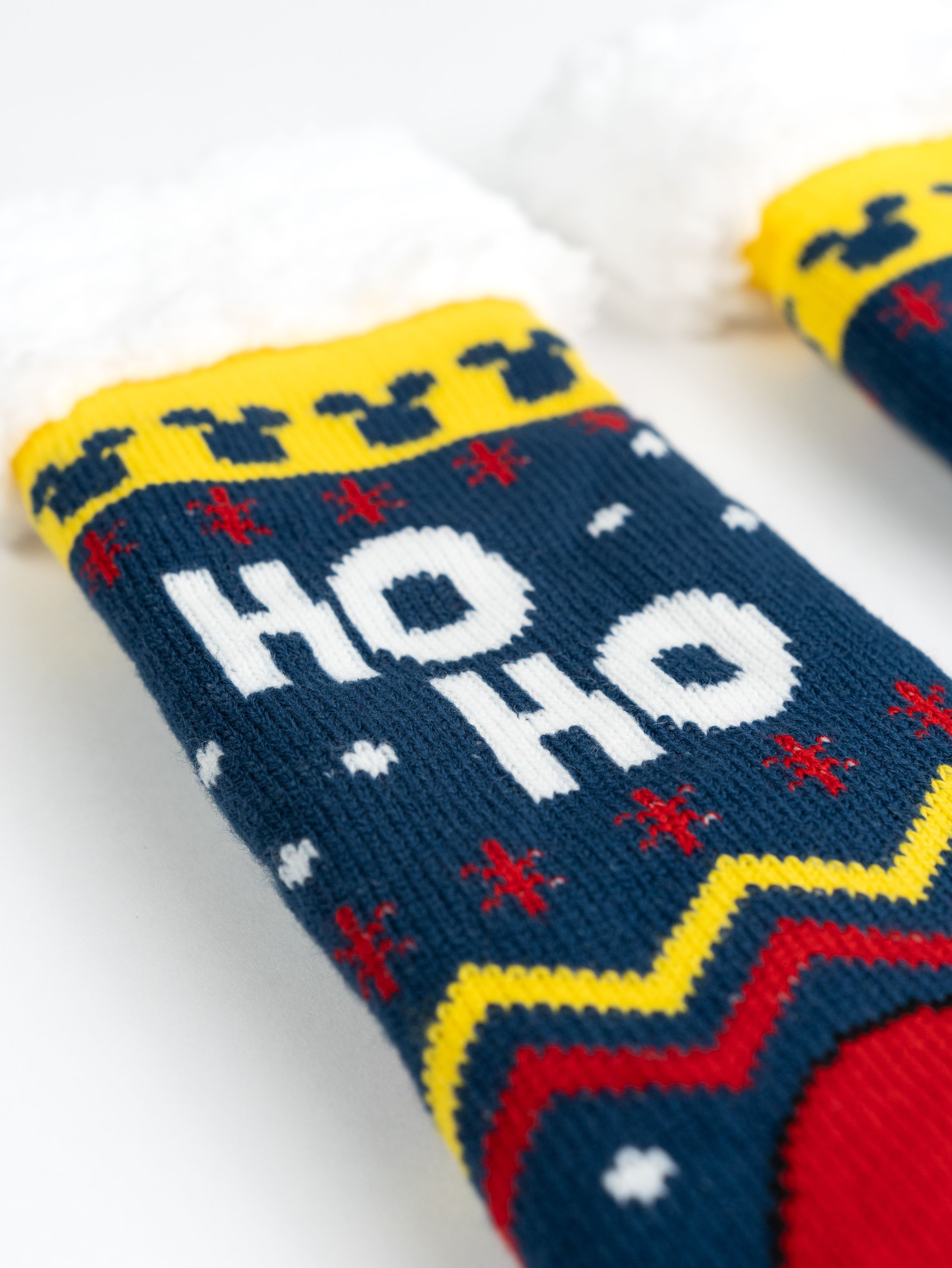 Zwei Weihnachtssocken, marineblau mit HO HO und roten und gelben Mustern, mit weißen, flauschigen Oberteilen.