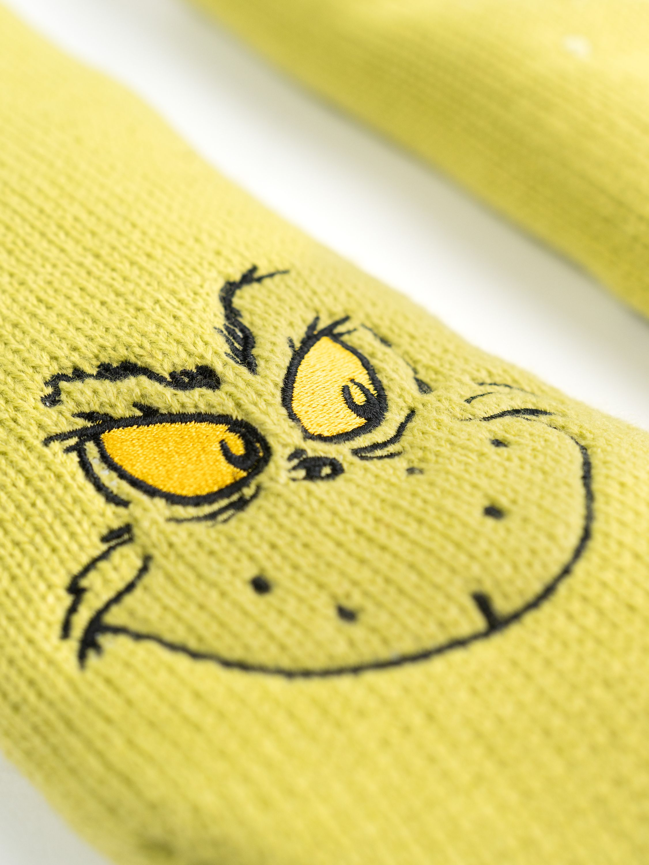 Nahaufnahme von grünen Grinch-Socken mit dem Gesicht und den Augen des Grinch mit gelben Iris.