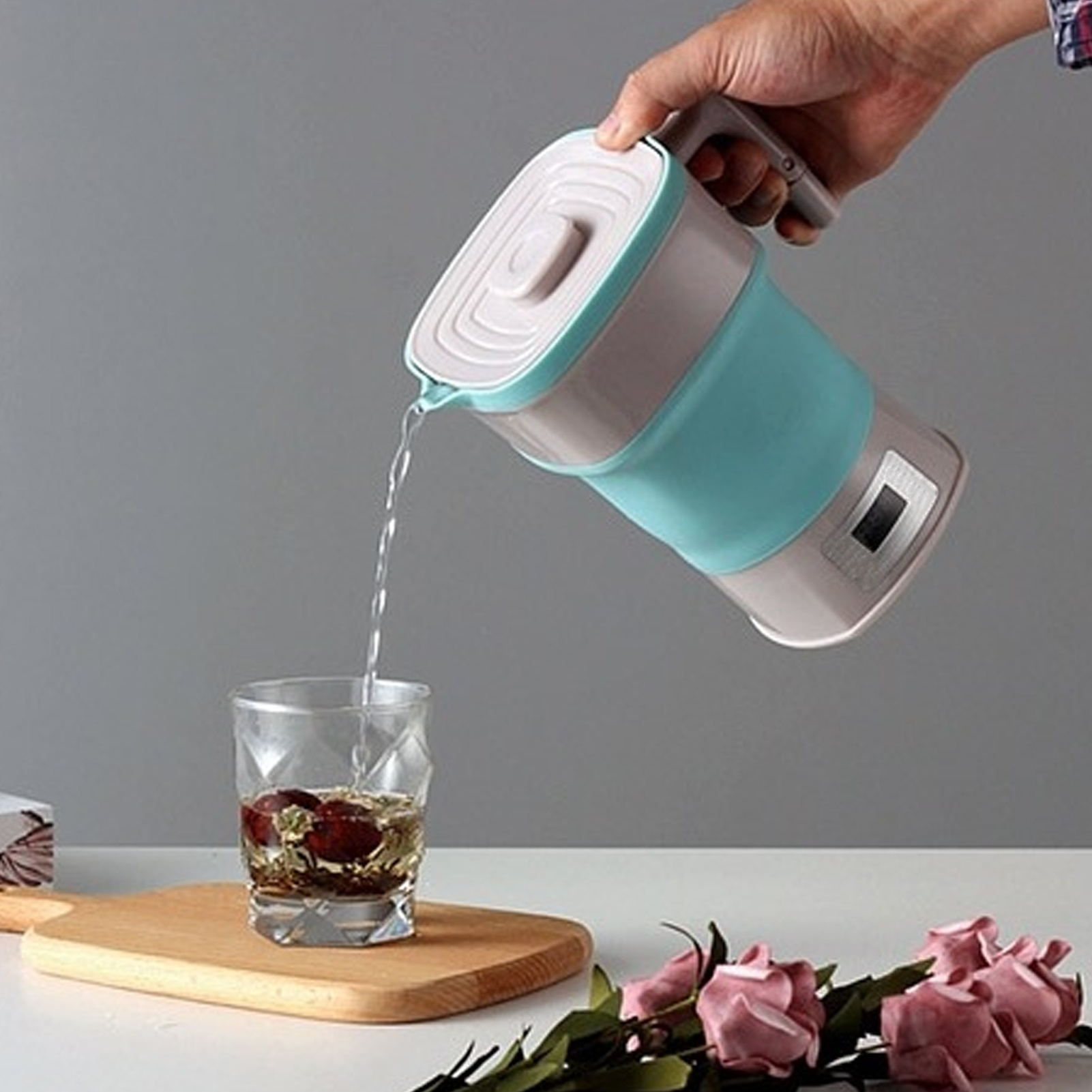 Ein faltbarer elektrischer Wasserkocher, der Wasser in ein Glas mit Früchten gießt.