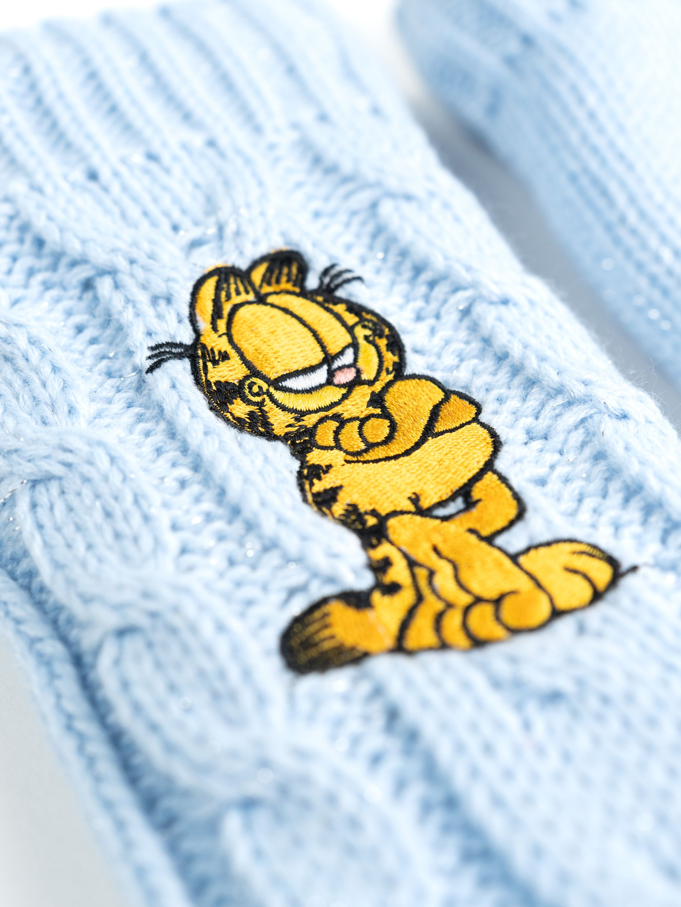 Nahaufnahme eines blauen Strickhandschuhs mit gesticktem Garfield-Charakter.