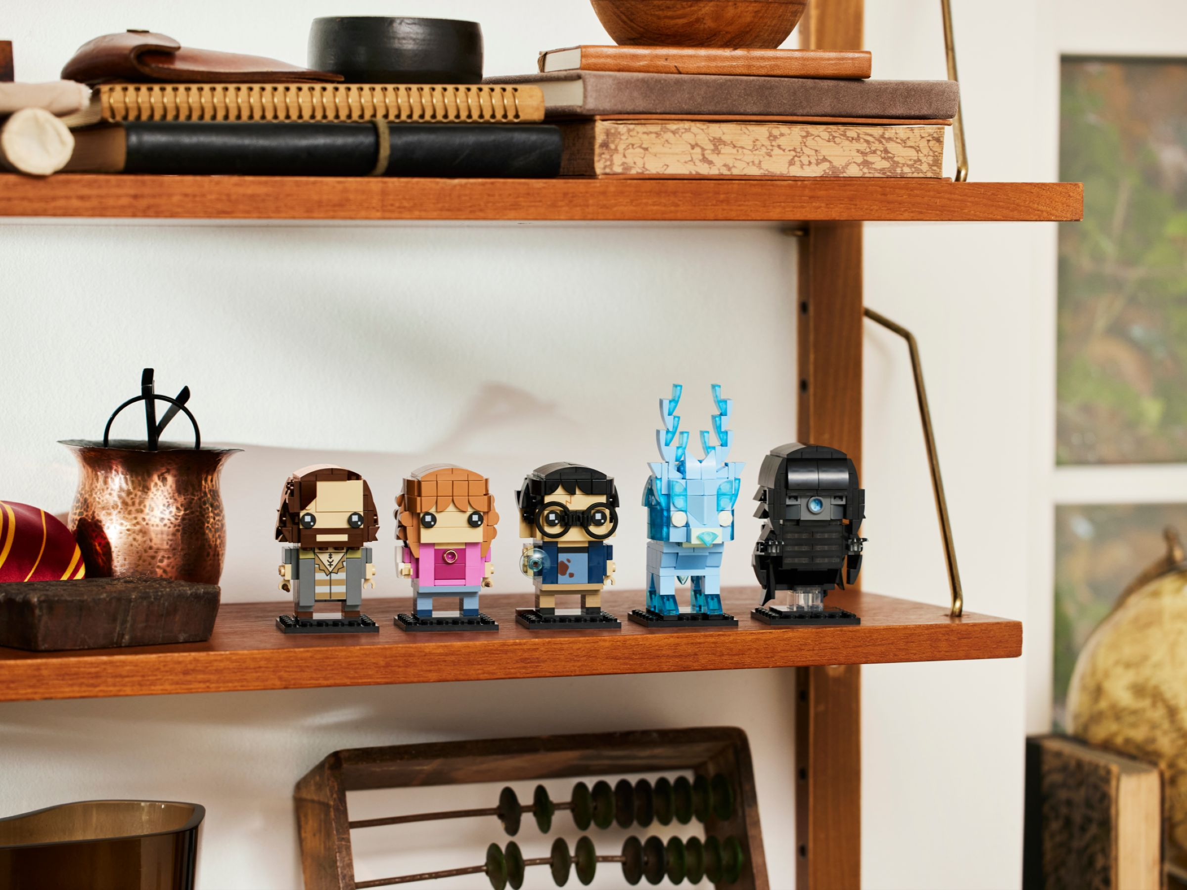Lego-Figuren von Charakteren auf einem Holzregal. Bücher und Deko im Hintergrund.