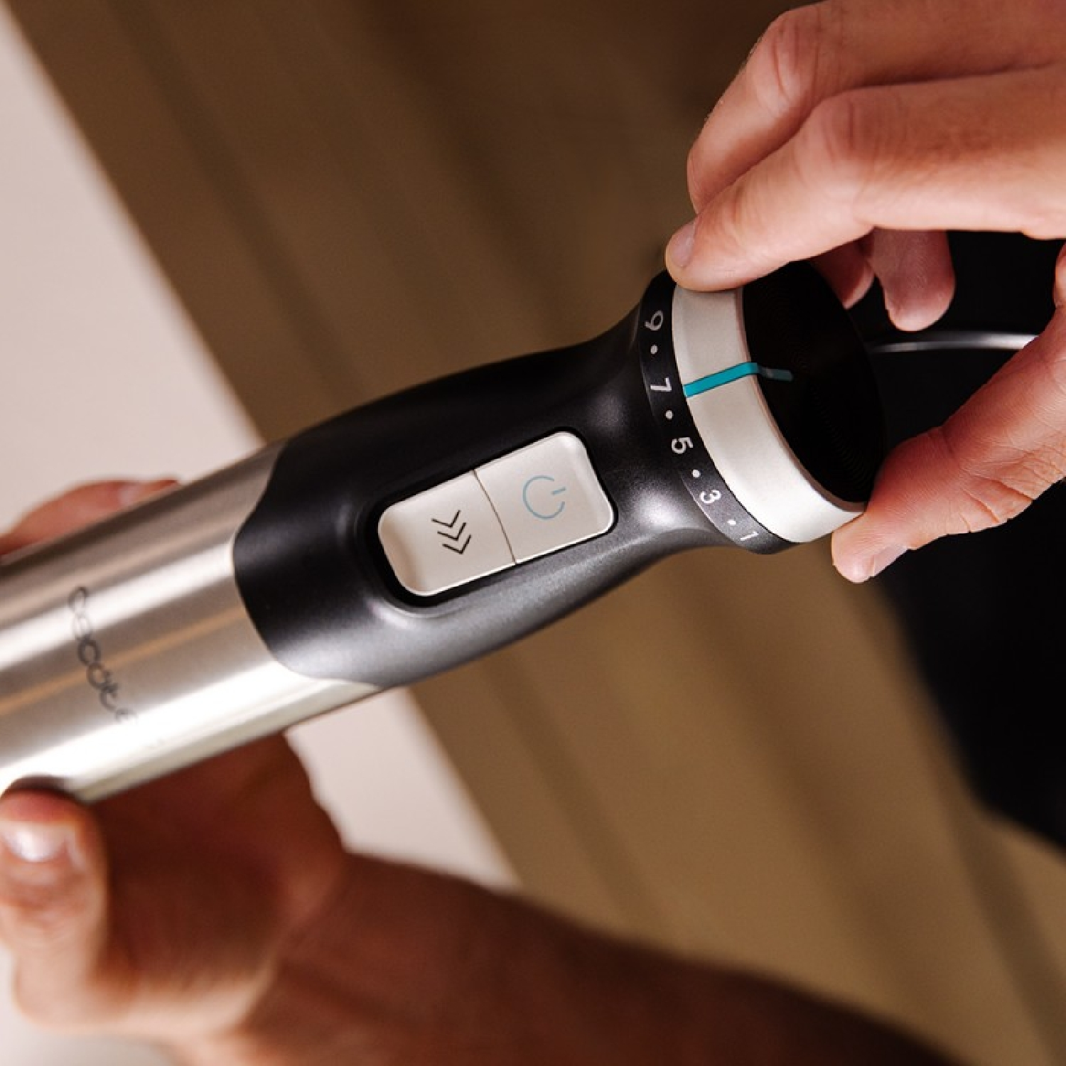 Zbliżenie blendera ręcznego z pokrętłem i przyciskami. Blender jest srebrny i czarny.