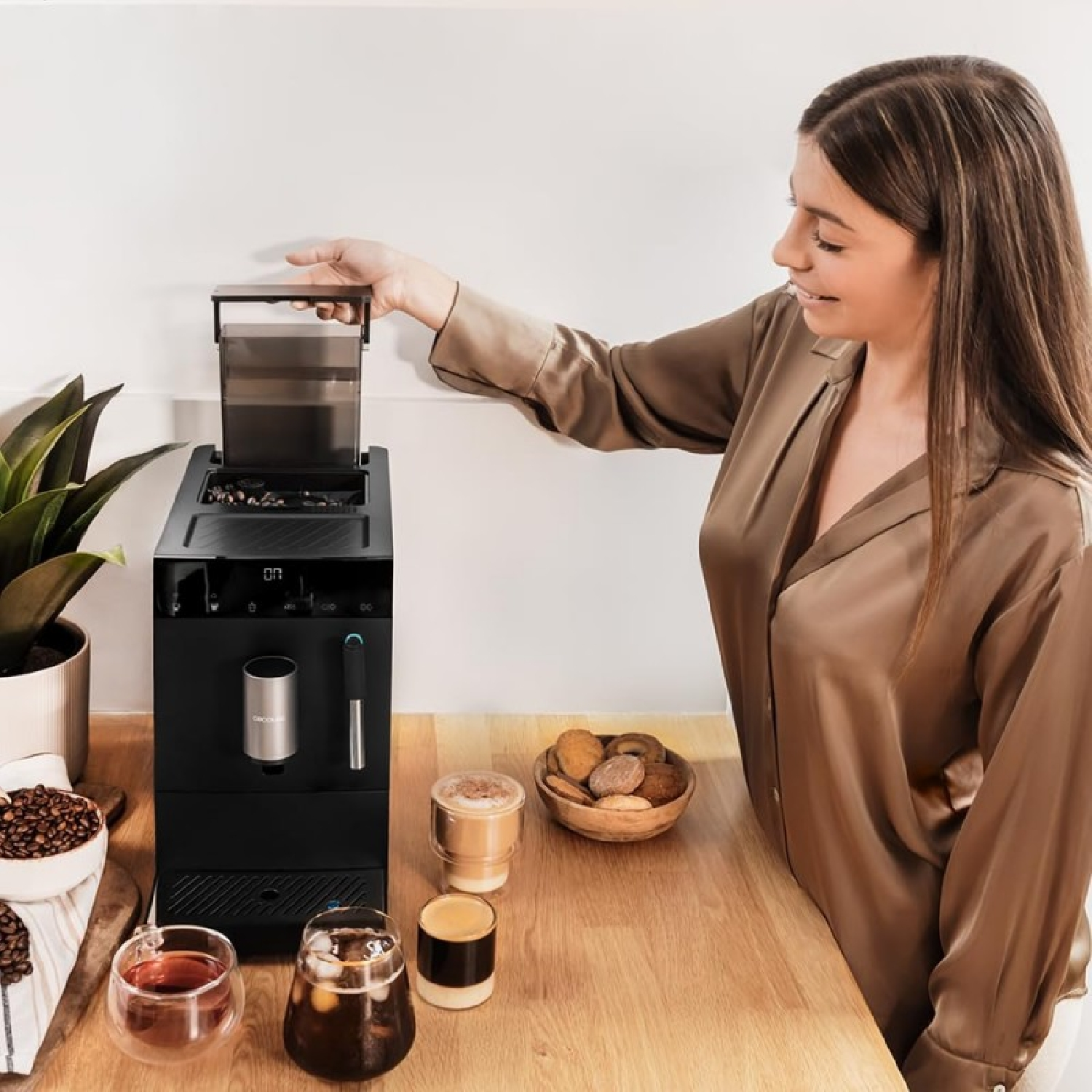 Donna che usa una macchina da caffè nera, prepara il caffè. Ci sono tazze da caffè e biscotti sul tavolo.