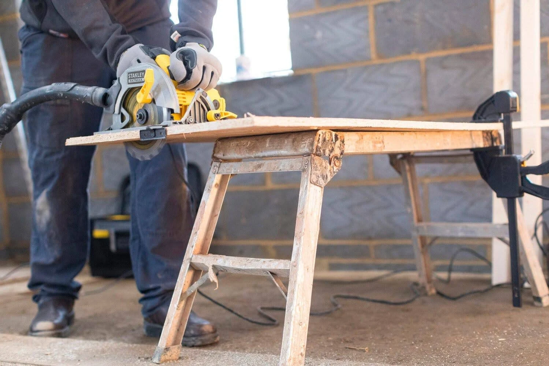 Een man zaagt een plank hout op een houten zaagbok.