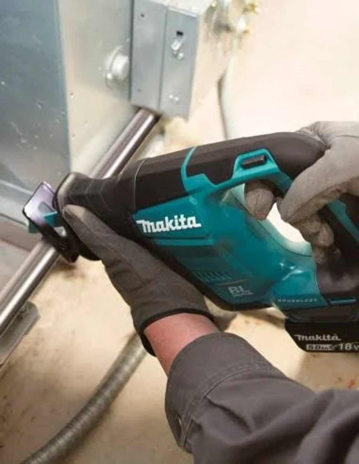 Una persona con guantes usa una sierra recíproca Makita verde azulado y negra en un objeto metálico.