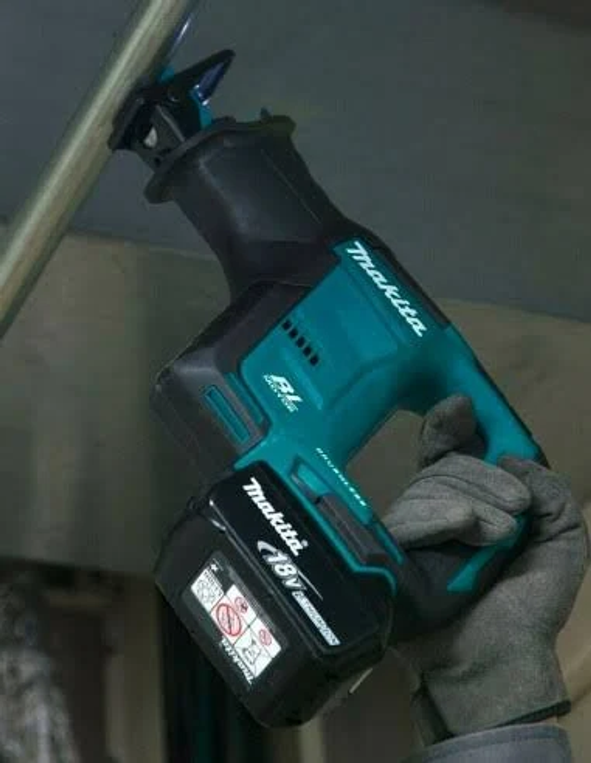 Persona sosteniendo una sierra recíproca Makita turquesa y negra, trabajando en un techo.