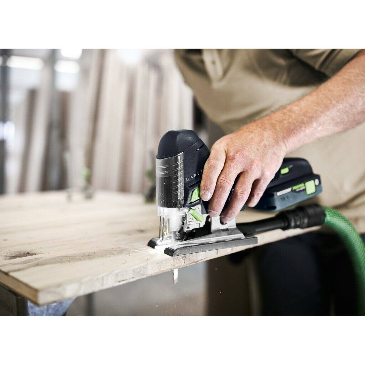 Osoba tnąca drewno czarną wyrzynarką. Widoczne wióry. Jasna powierzchnia drewniana.