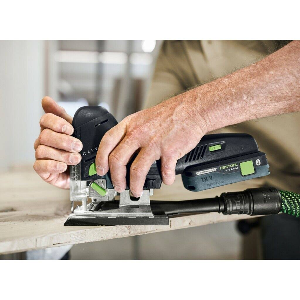 Osoba używająca czarno-zielonej szlifierki na drewnianej powierzchni. Dołączona jest rura odkurzacza.