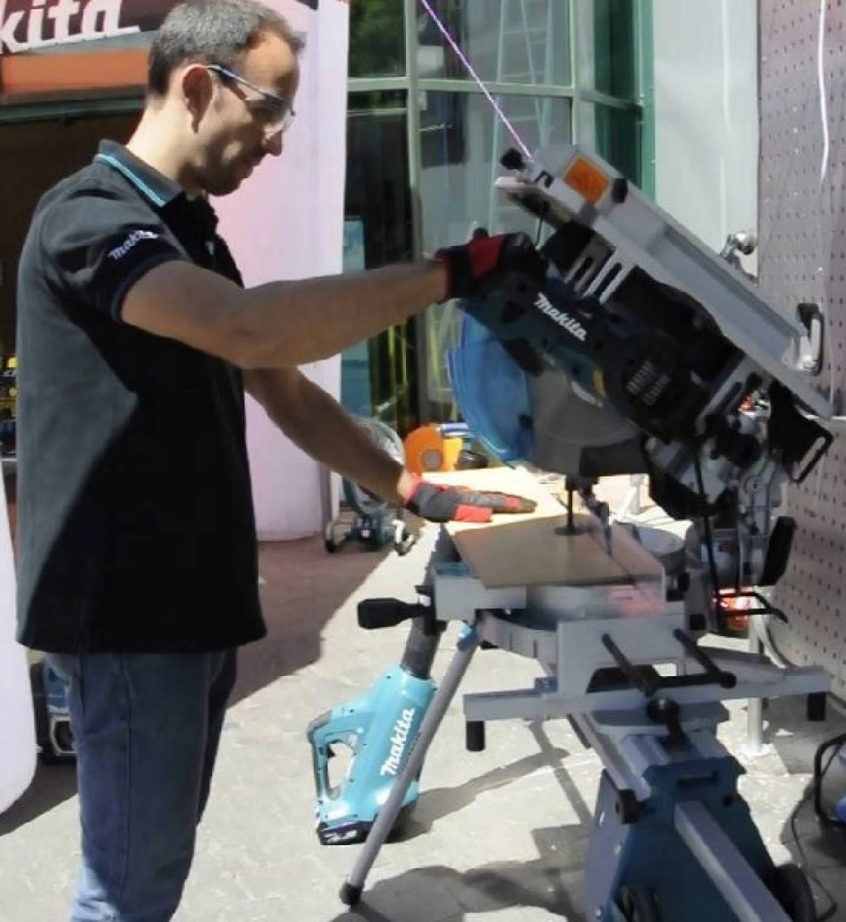 Un hombre usa una sierra Makita para cortar madera. Lleva gafas de seguridad y guantes.