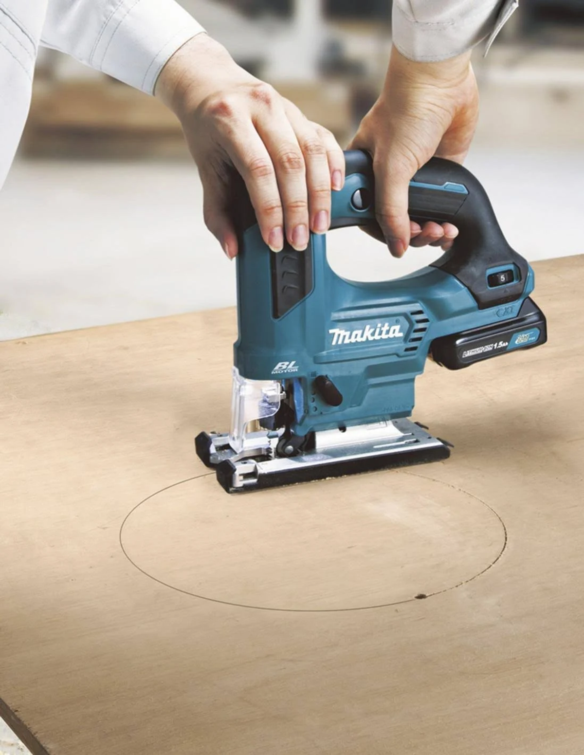 Una persona usando una sierra de calar Makita color turquesa para cortar un círculo en una tabla de madera.