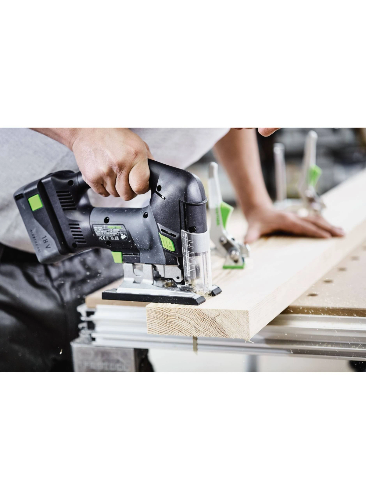 Osoba używa czarno-zielonej wyrzynarki do cięcia drewnianej deski na stole warsztatowym.