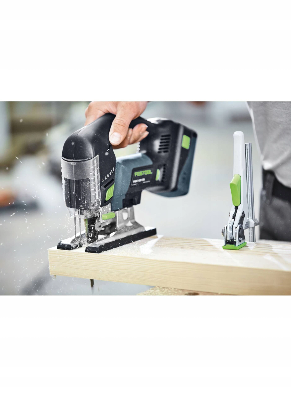 Osoba używająca czarno-zielonej wyrzynarki na drewnianej desce. Widoczne trociny.