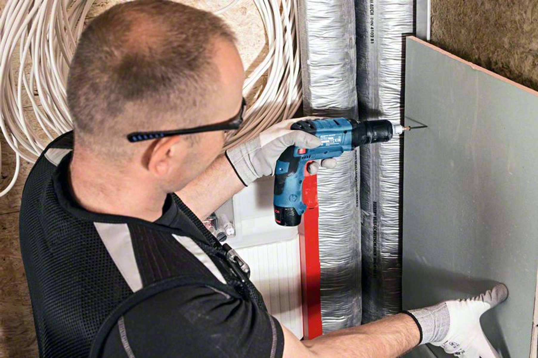 Mężczyzna używający niebieskiej wiertarki akumulatorowej do wkręcania w ścianę.