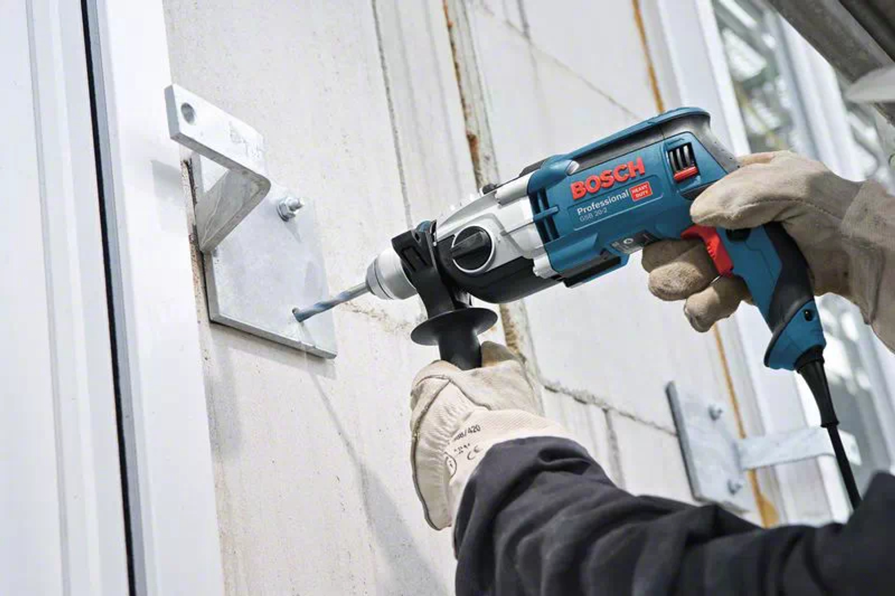 Eine Person benutzt eine Bosch-Bohrmaschine, um in eine Metallplatte an einer Wand zu bohren.