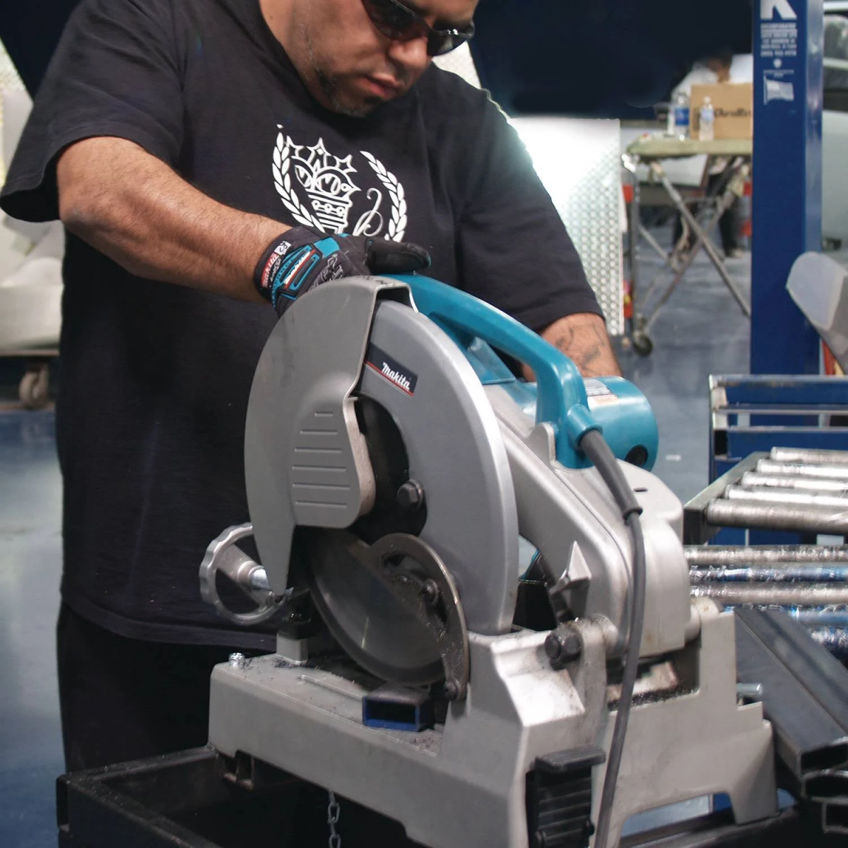 Mann in schwarzem Hemd, der eine Makita Trennsäge zum Schneiden von Metallstangen in einer Werkstatt benutzt.