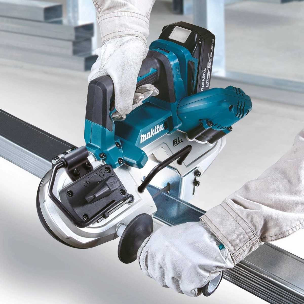 Osoba używająca piły taśmowej Makita do cięcia metalu, w rękawicach, na tle metalowej ramy.
