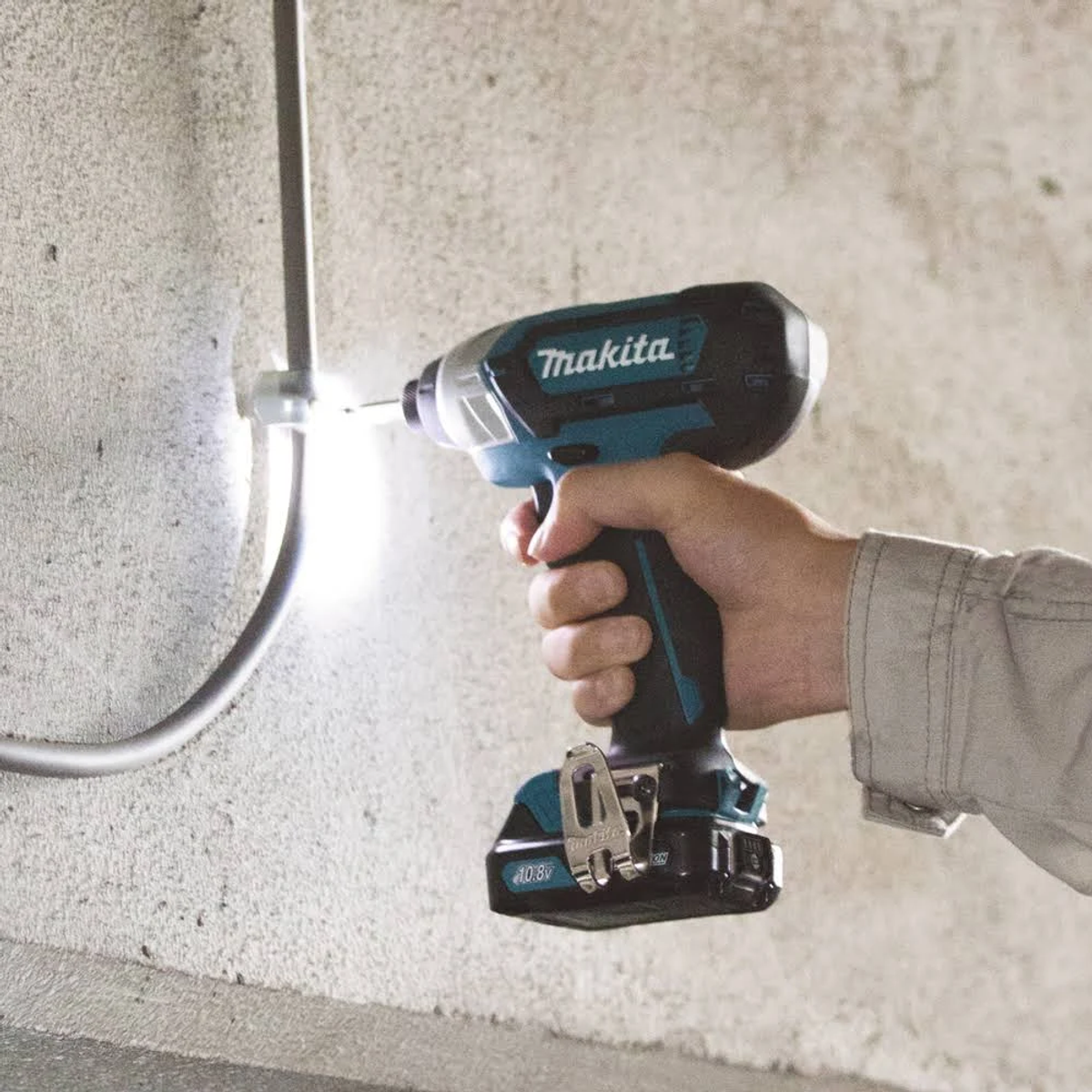 Avvitatore a impulsi Makita utilizzato per avvitare in un tubo metallico. Un muro di cemento sullo sfondo.