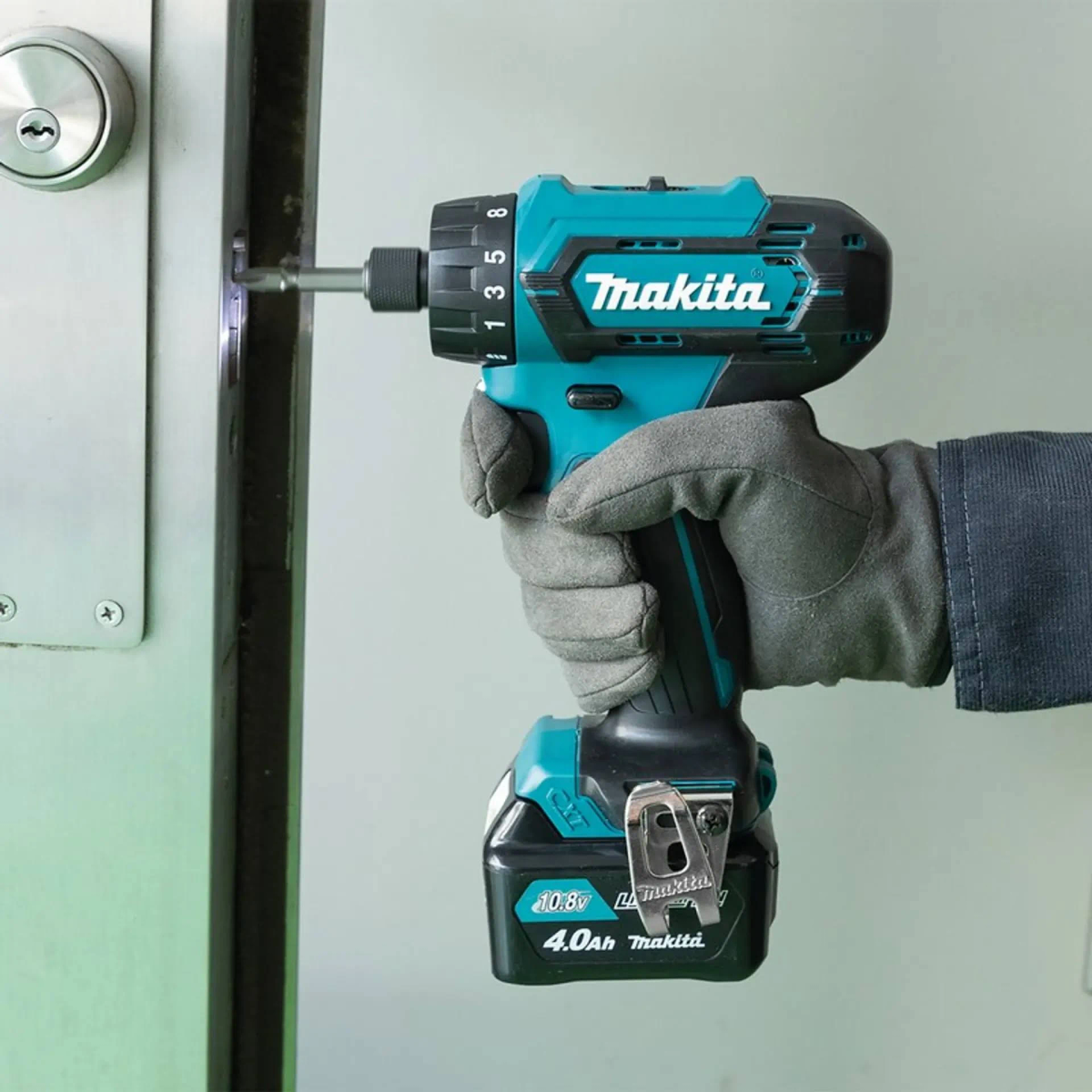 Persona usando un taladro inalámbrico Makita turquesa y negro para atornillar en un marco de puerta.