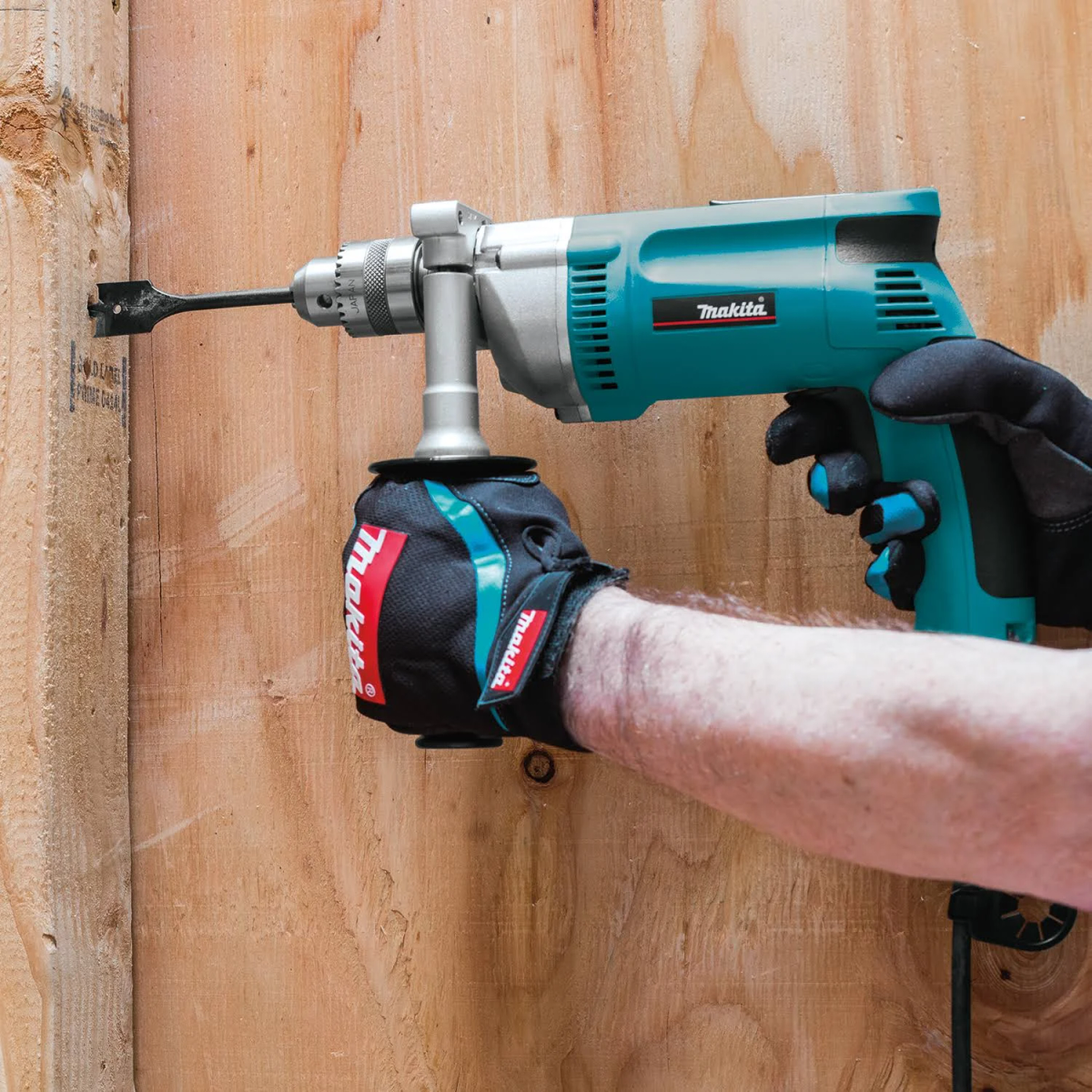 Una persona che usa un trapano Makita turchese per forare una recinzione di legno.