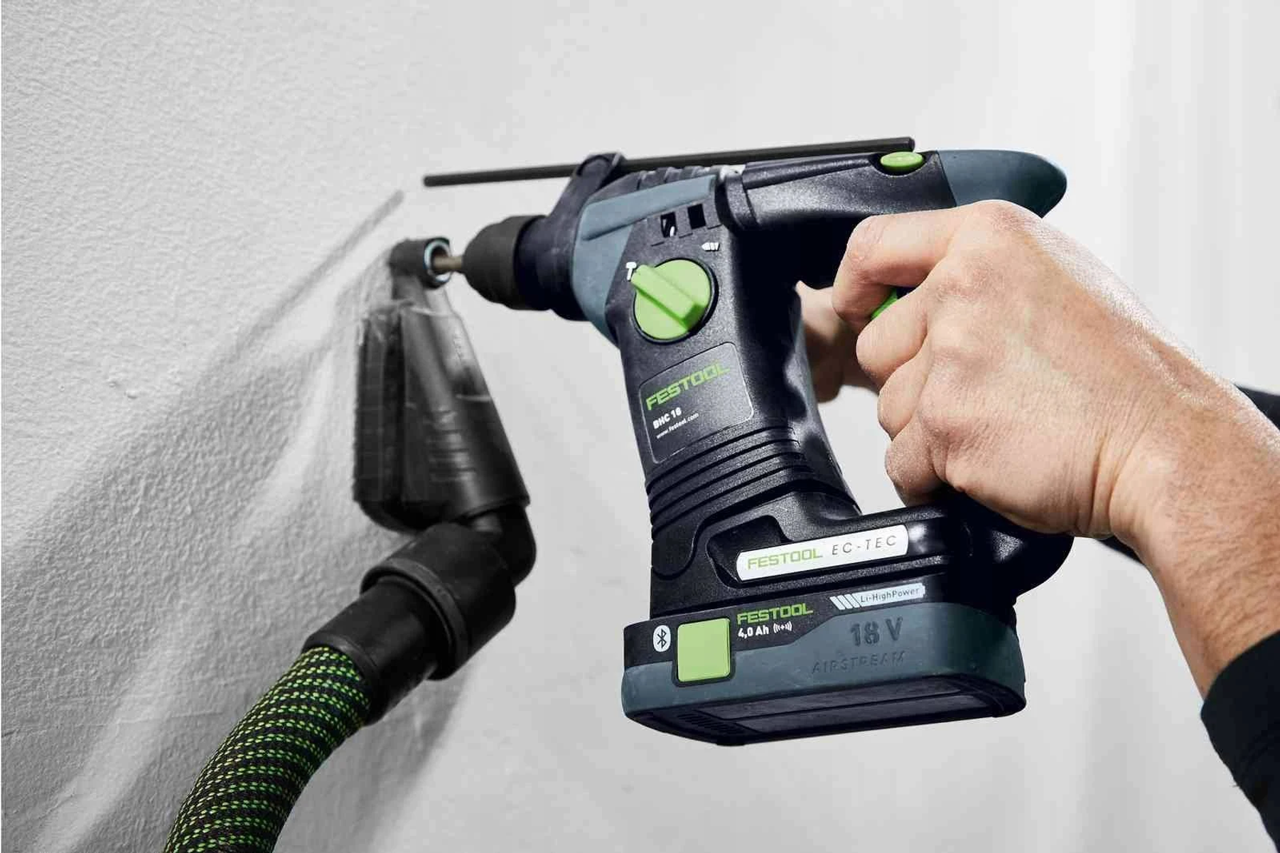Una persona fora un muro con un trapano elettrico Festool mentre indossa occhiali protettivi e tappi per le orecchie.