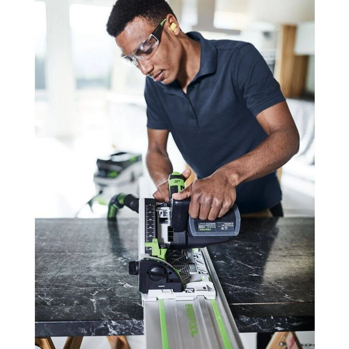 Uomo con occhiali usa una sega a binario Festool su superficie in marmo scuro con guida verde.