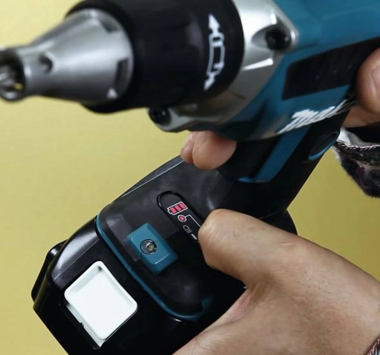 Zbliżenie dłoni trzymającej czarno-turkusowe elektronarzędzie, na żółtym tle.