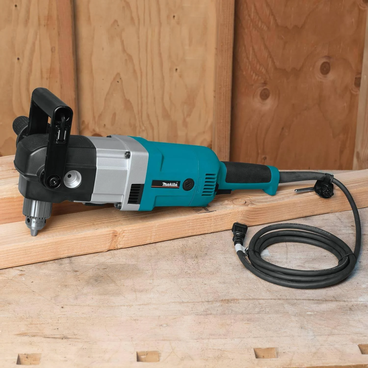 Una amoladora angular Makita turquesa sobre una superficie de madera, con un cable de alimentación negro. Se está trabajando en un trozo de madera.