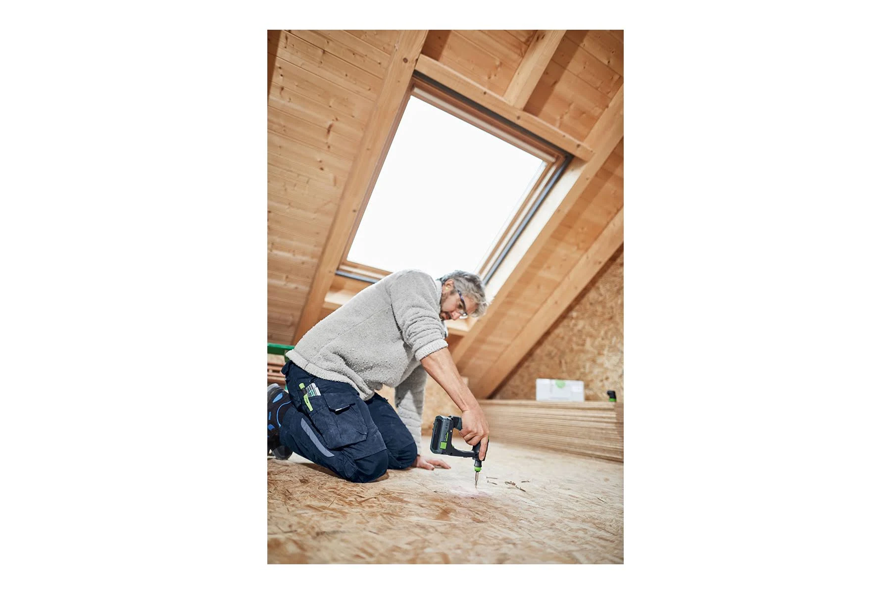 Osoba klęcząca, używająca wiertarki akumulatorowej do wiercenia w drewnie.