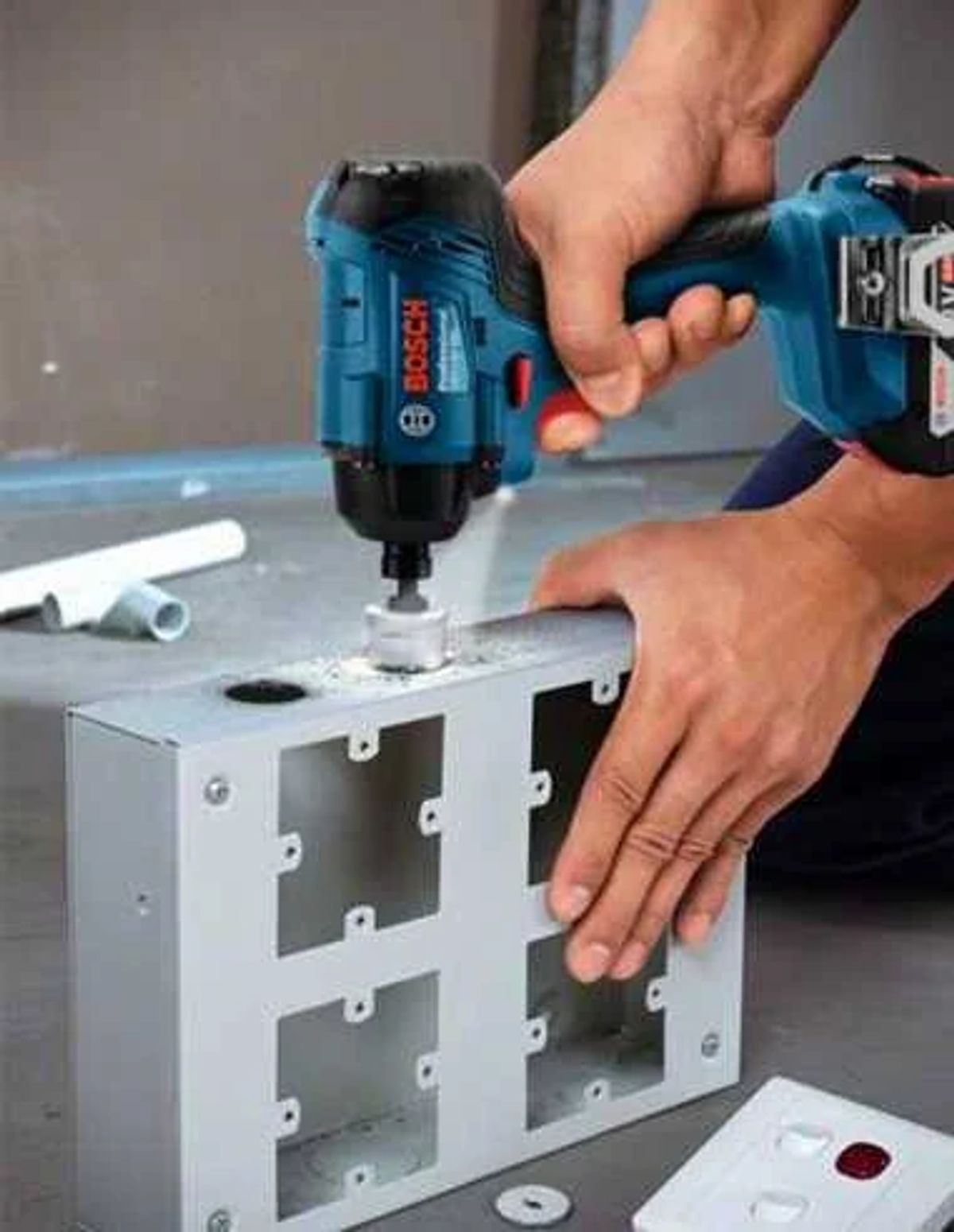 Una persona usando un taladro para hacer agujeros en una caja de metal, con otra caja cerca.