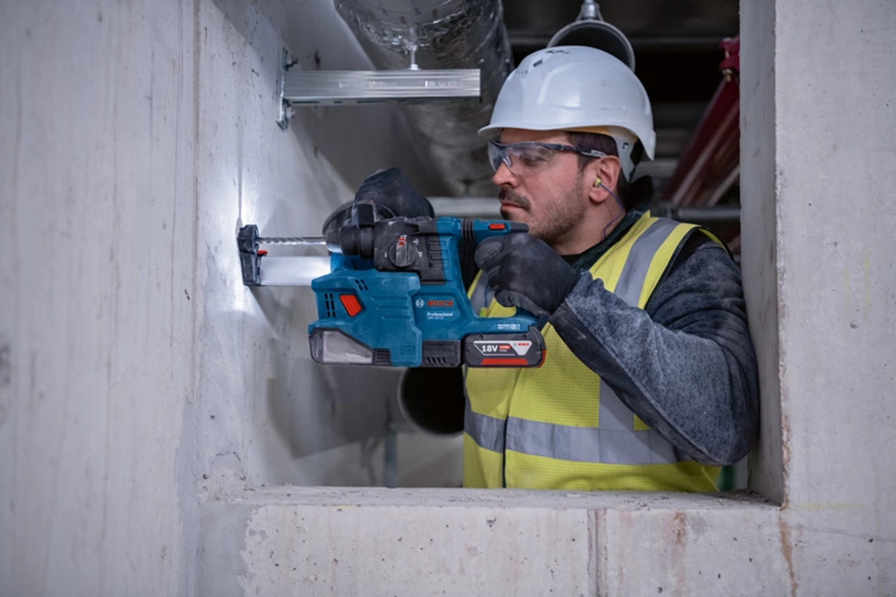 Un trabajador de la construcción usando un taladro en una pared de concreto, usando equipo de seguridad.
