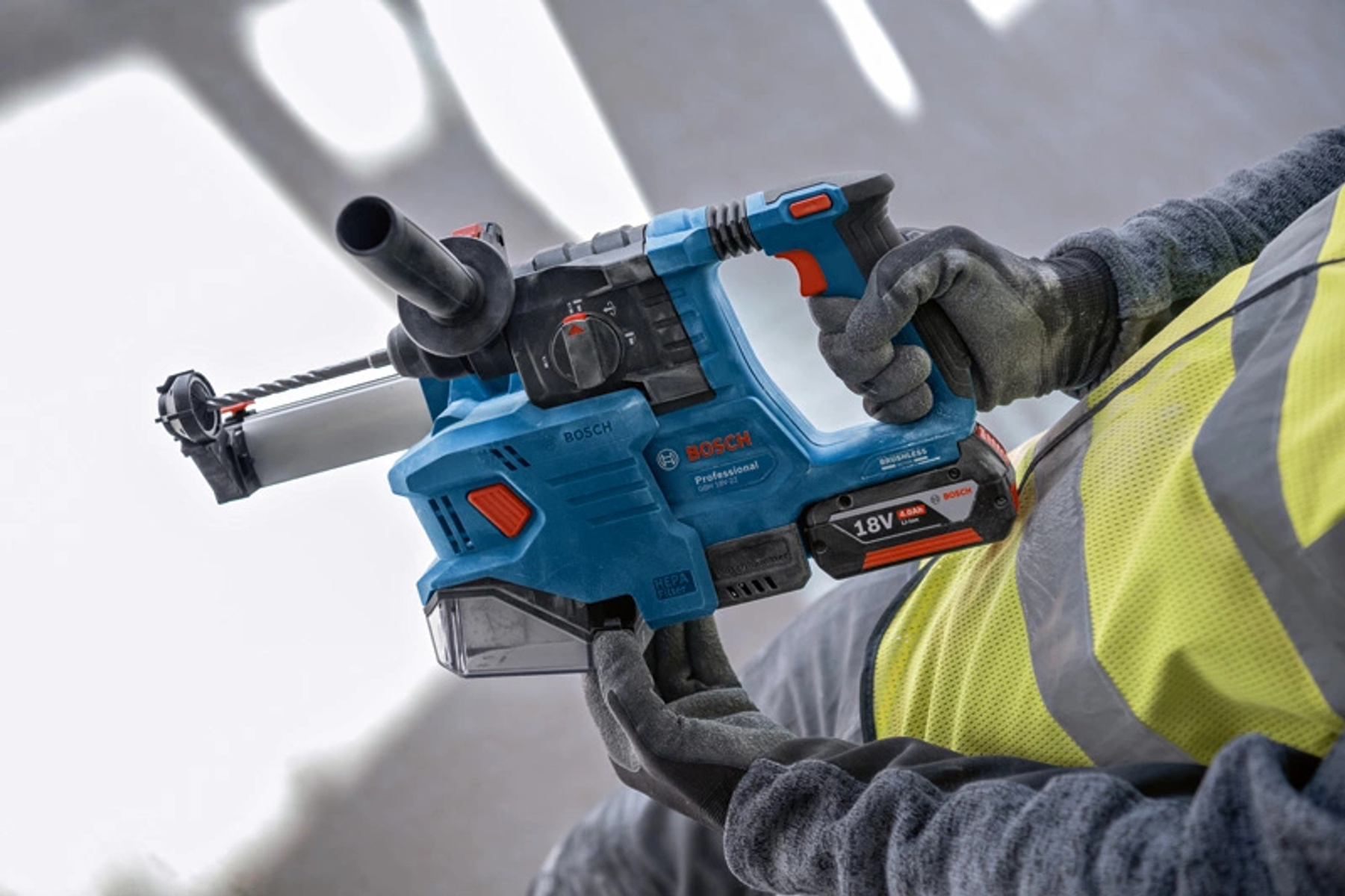Una persona usa un taladro Bosch azul, primer plano. El taladro está cerca de una pared blanca.