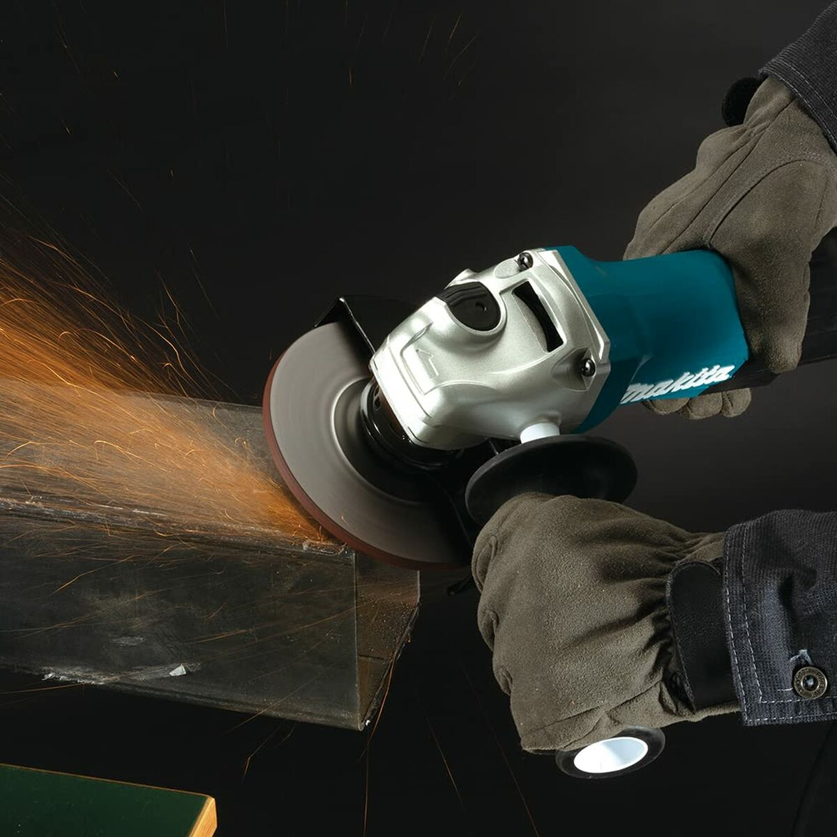 Persona amolando metal con una amoladora Makita, chispas contra un fondo oscuro.