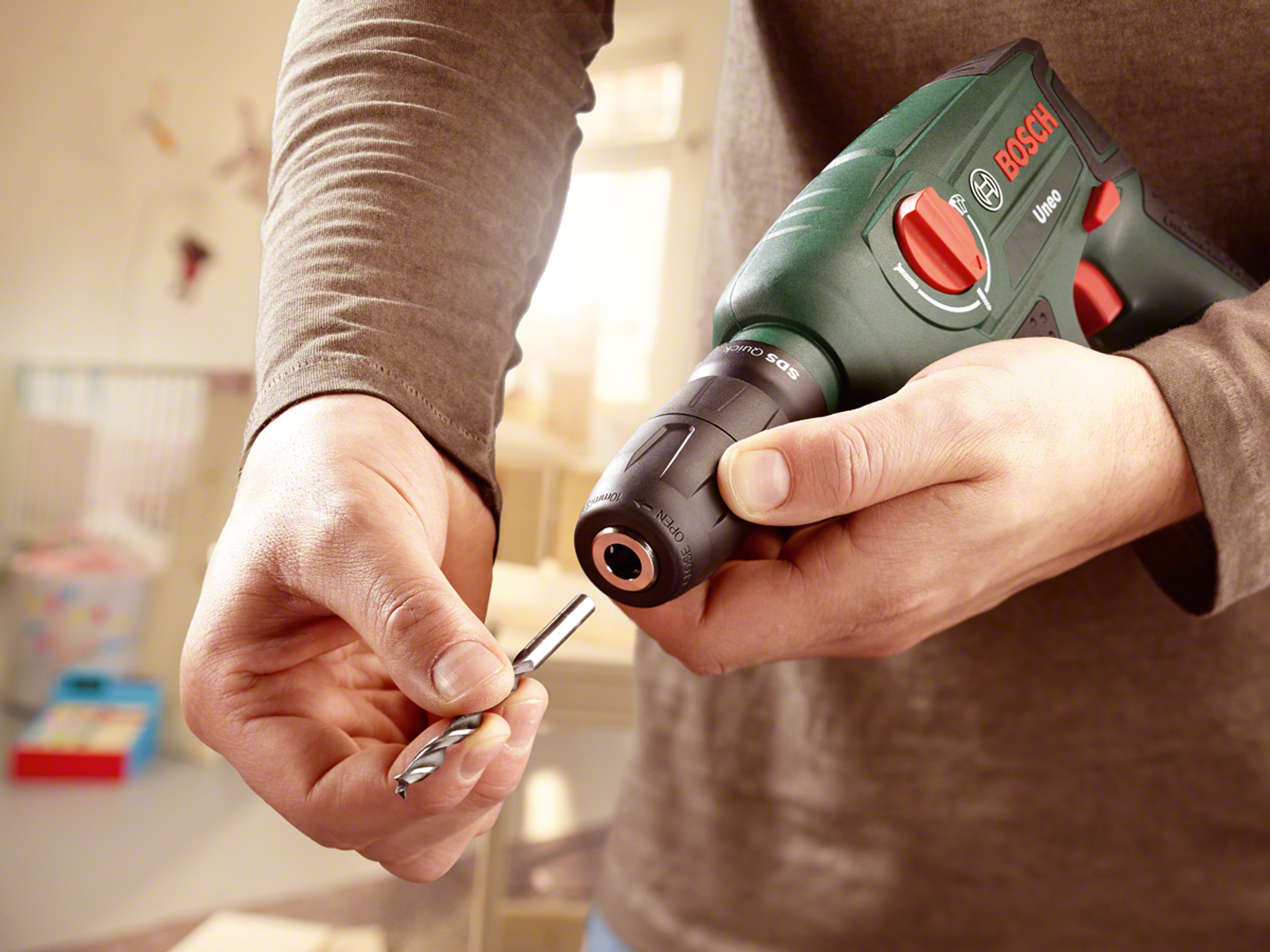 Osoba trzymająca wiertarkę i wiertło. Wiertarka jest zielona i czarna.