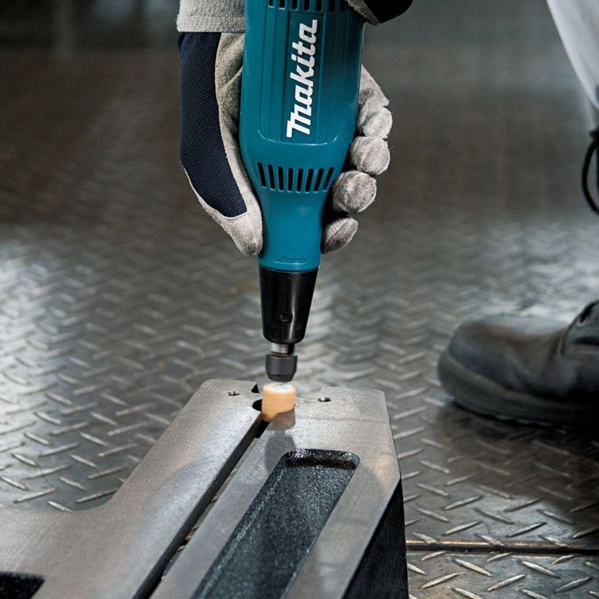 Una persona con guantes, usando una amoladora Makita en una superficie metálica.