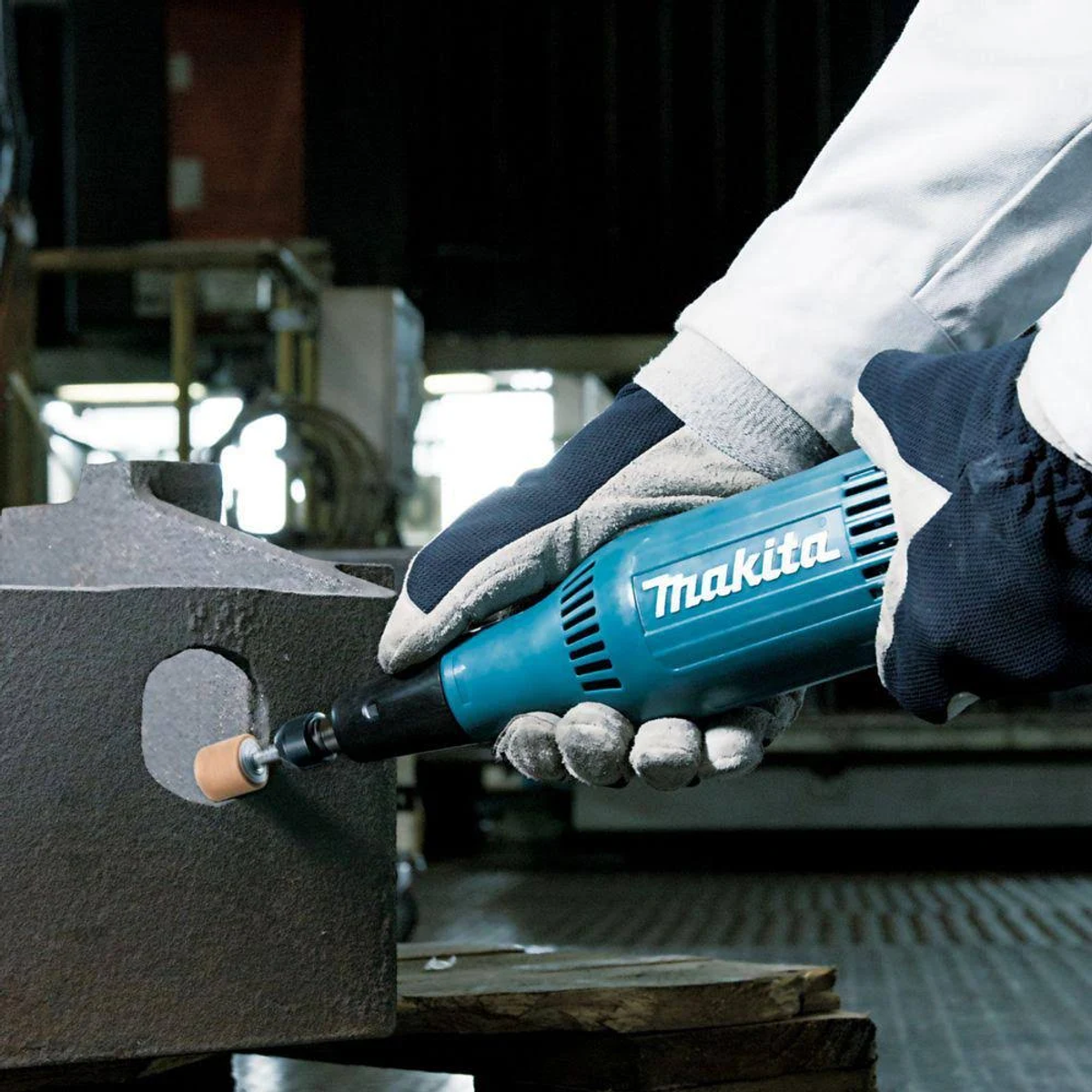 Una persona usando una amoladora Makita en un objeto de metal con guantes.